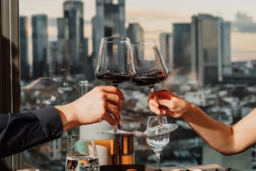 a group of people holding wine glasses at a table with food and a city view