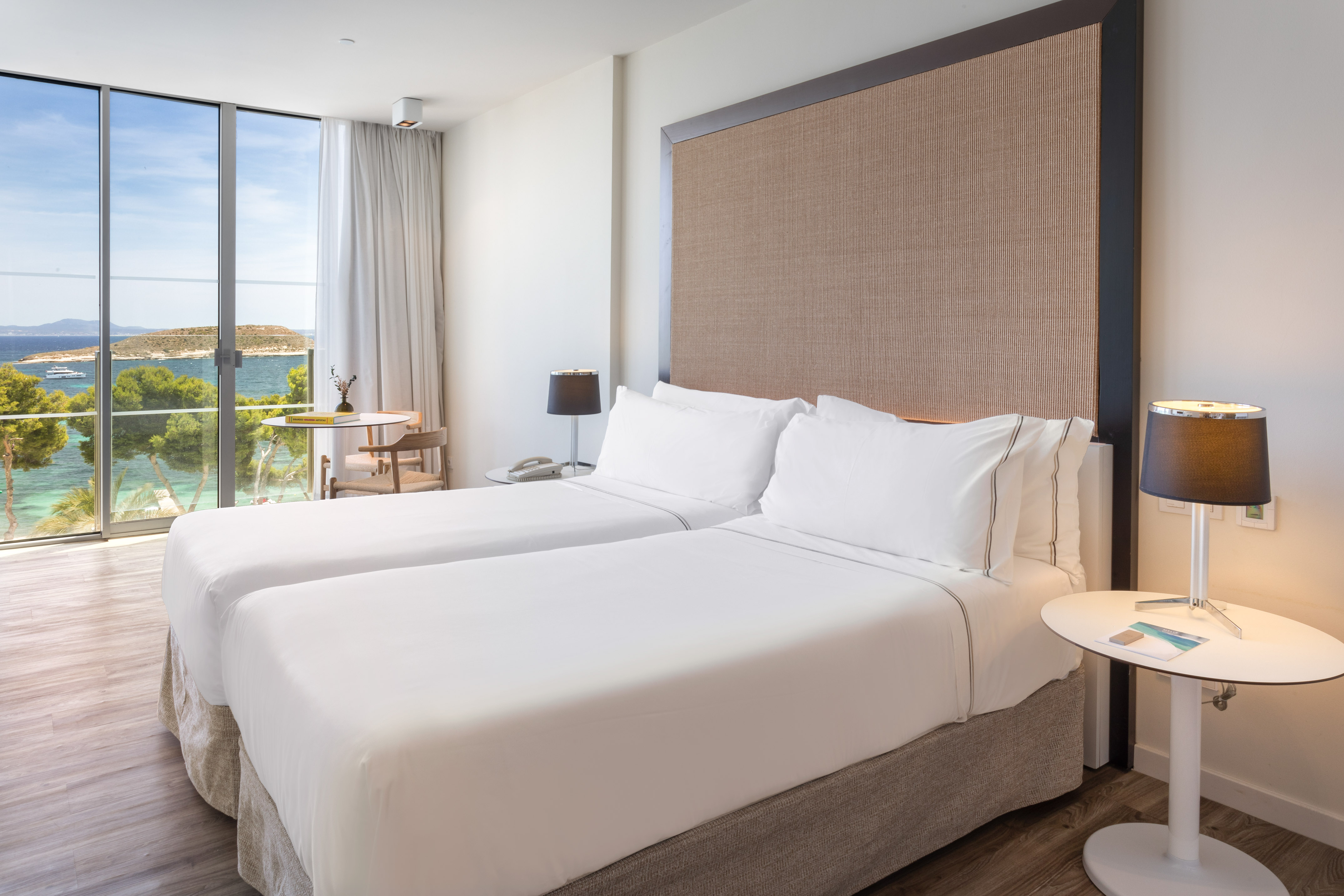 Modern hotel room with twin beds and panoramic sea view.