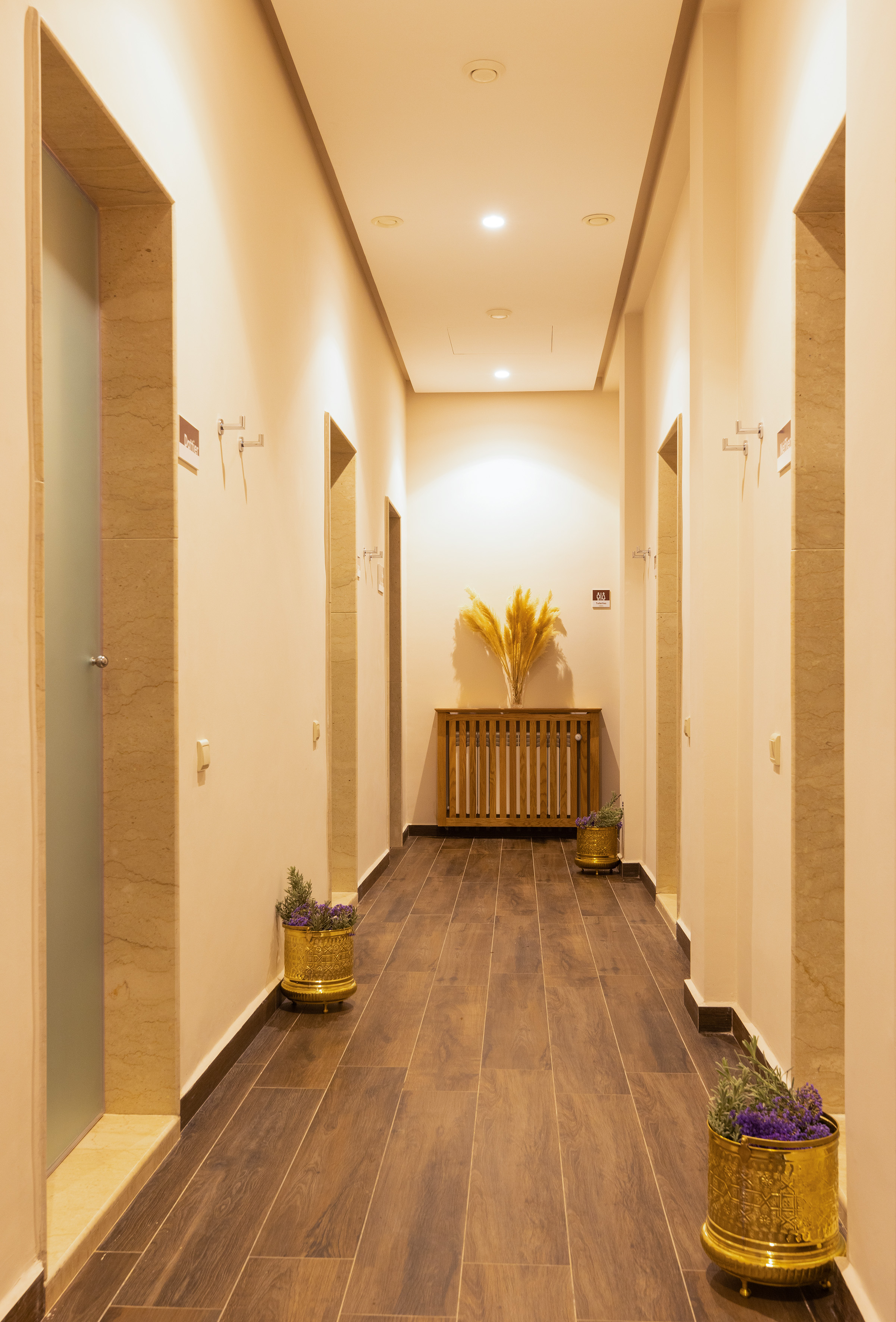 Warmly lit spa hallway with wood floor, decorative gold planters, and pampas grass.