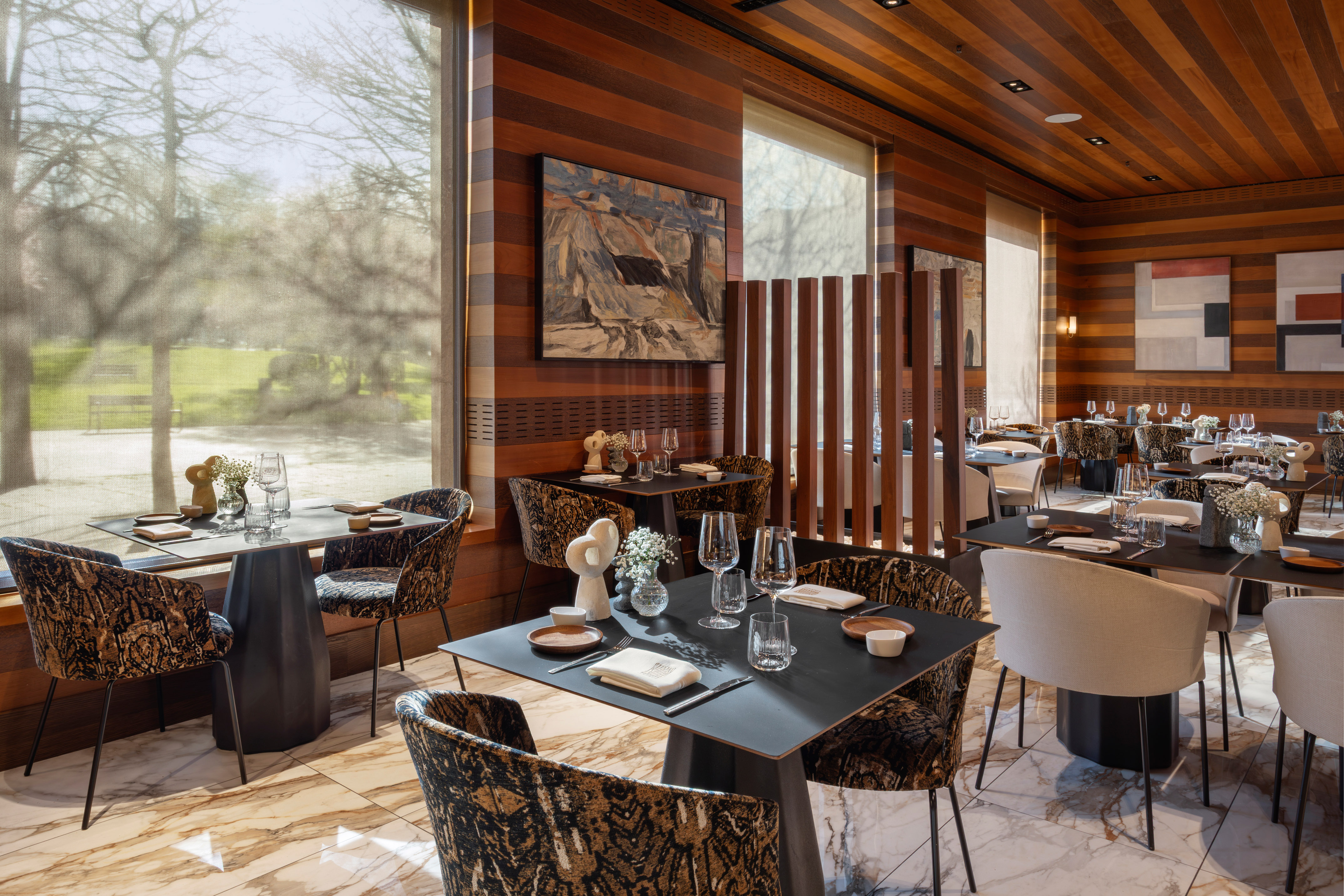 Elegant modern restaurant dining room with wooden decor and park view.