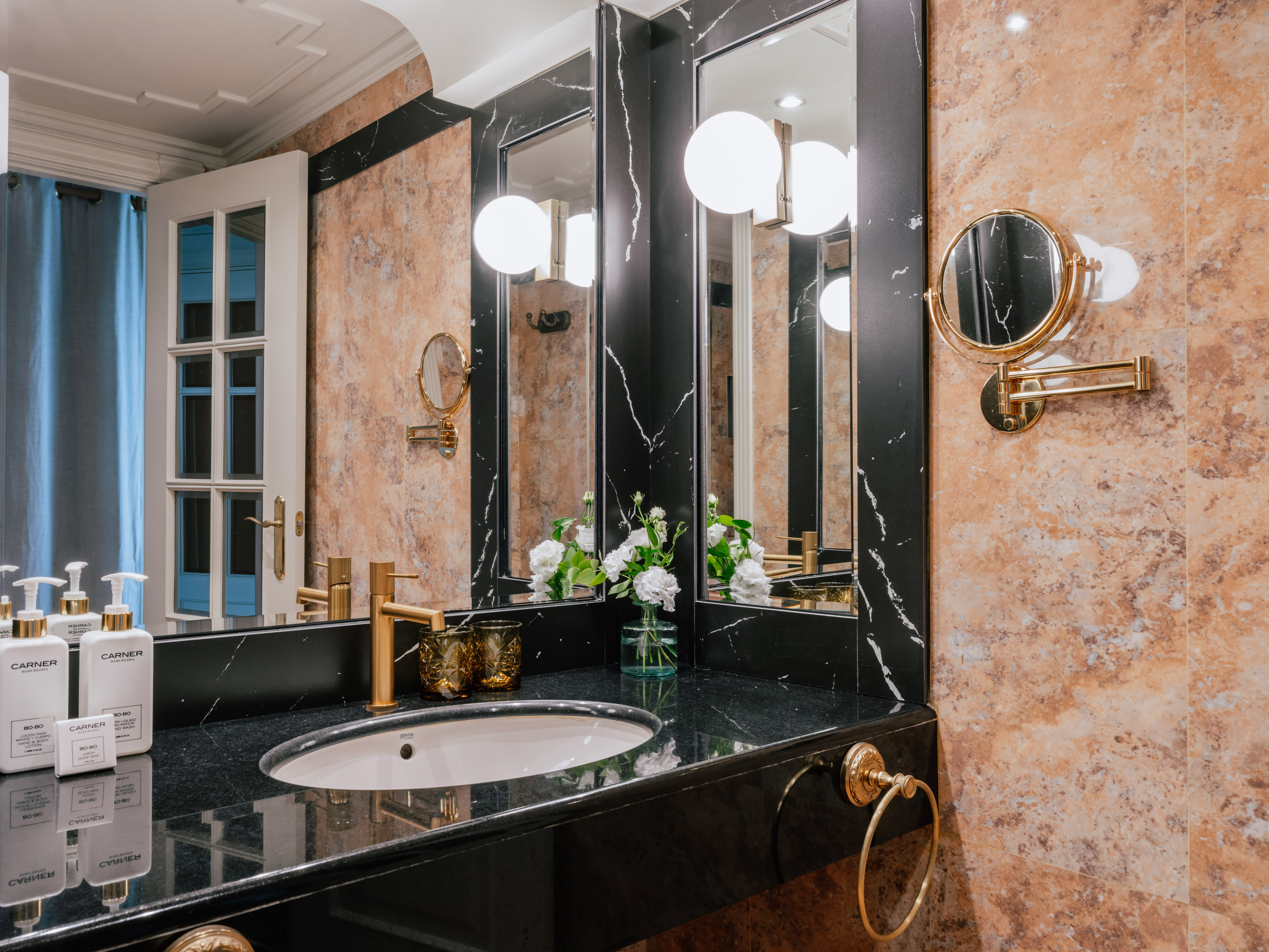 Luxury black marble bathroom vanity with gold fixtures, mirrors, and stone walls.