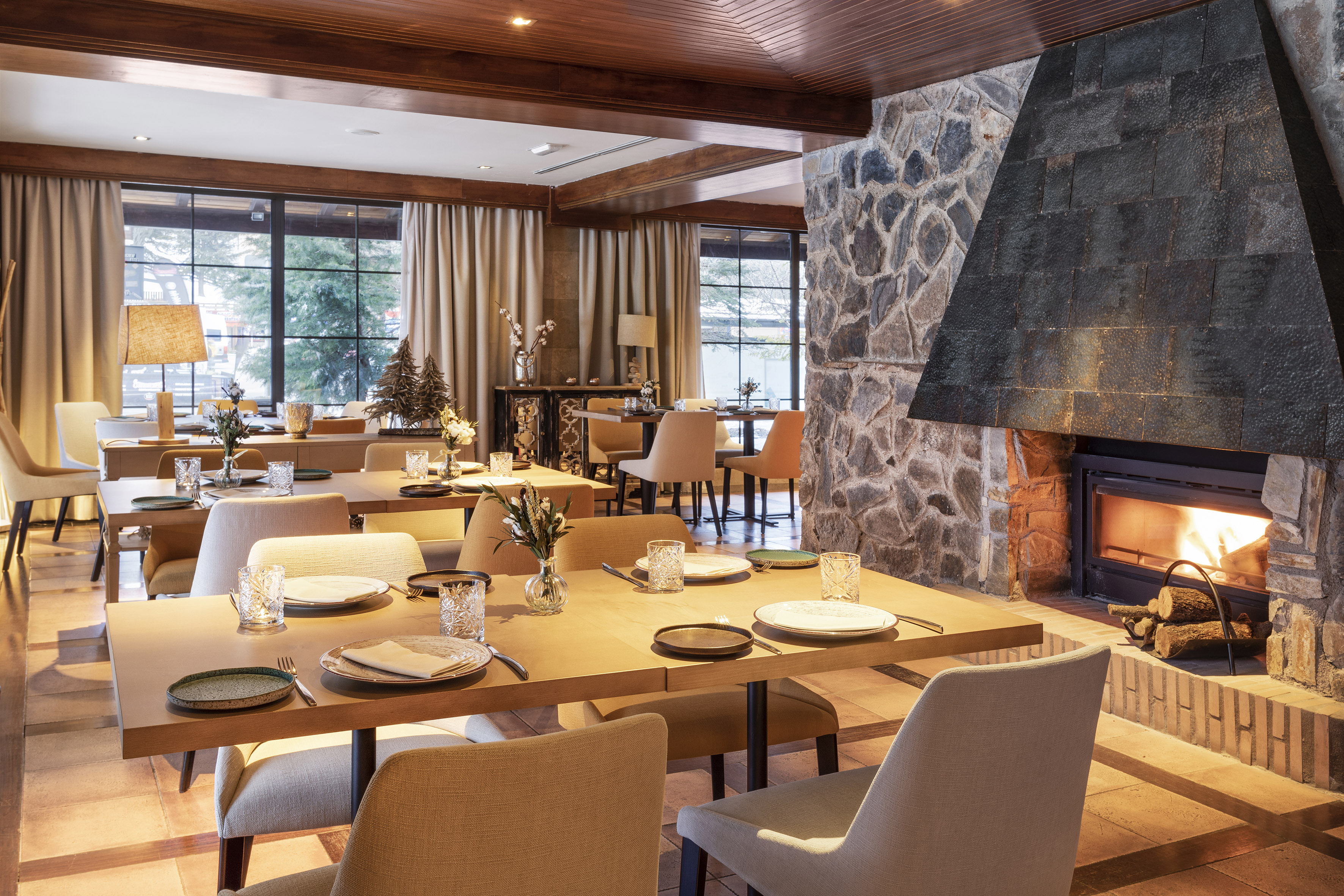 Restaurant dining room with stone fireplace, wooden ceiling, and set tables.