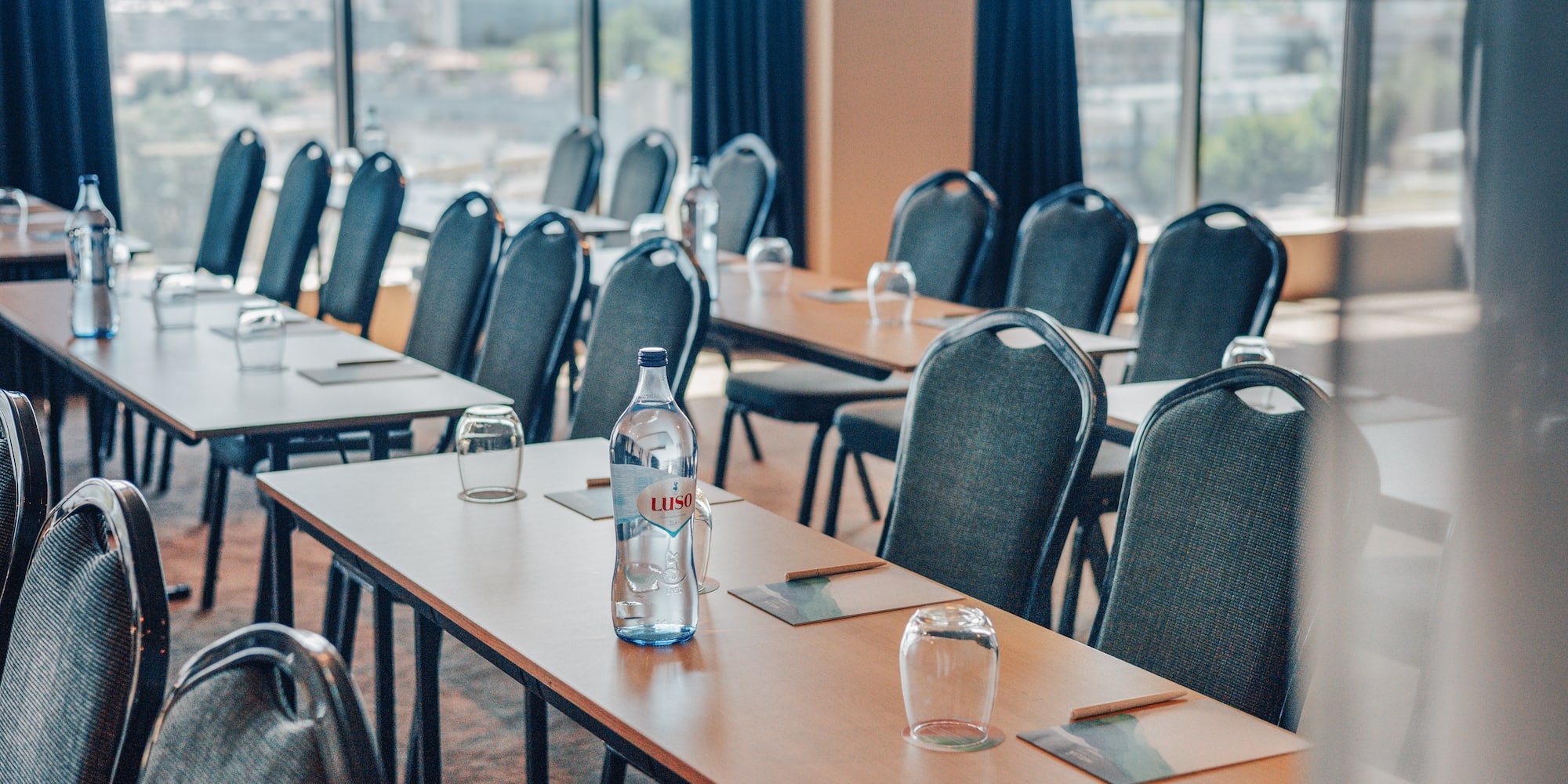 Empty meeting room with tables, chairs, water bottles, and a cityscape view.