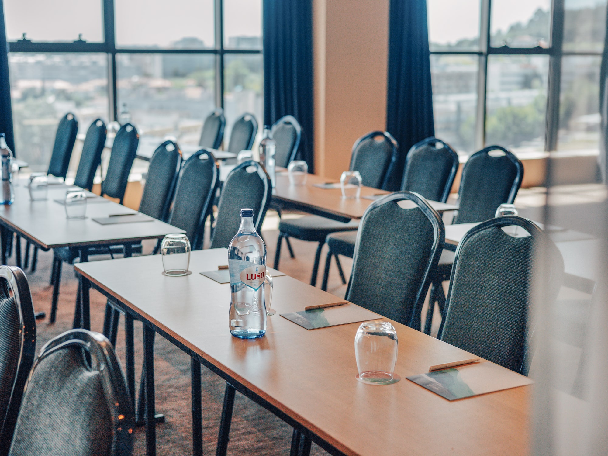 Conference room with tables, chairs, water bottles, and sunlit windows.