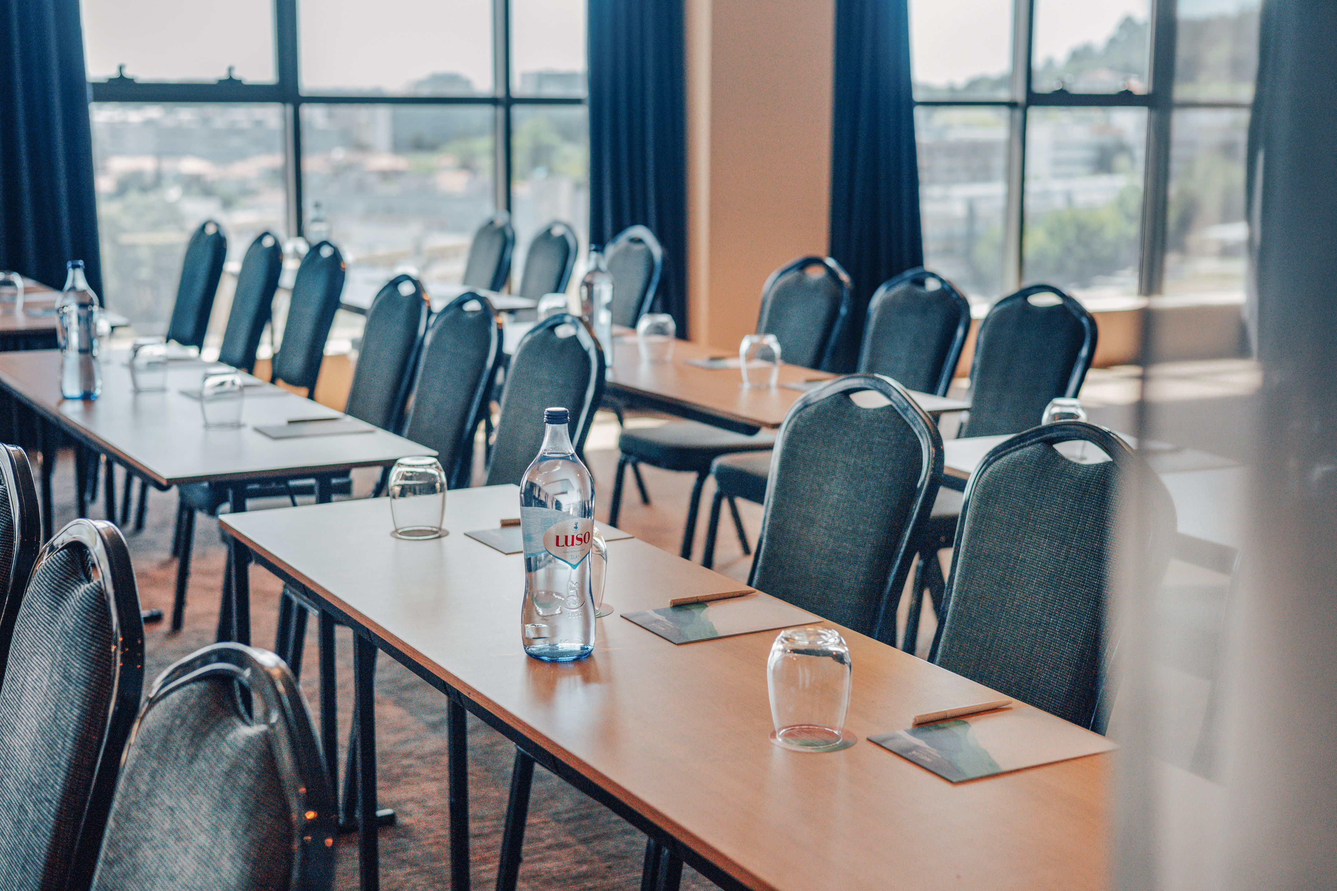 Empty meeting room with tables, chairs, water bottles, and a cityscape view.
