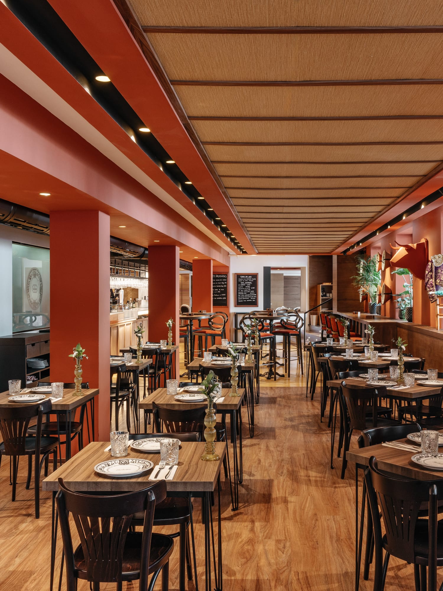 Modern restaurant dining room with orange walls, wooden tables, and bull head decor.