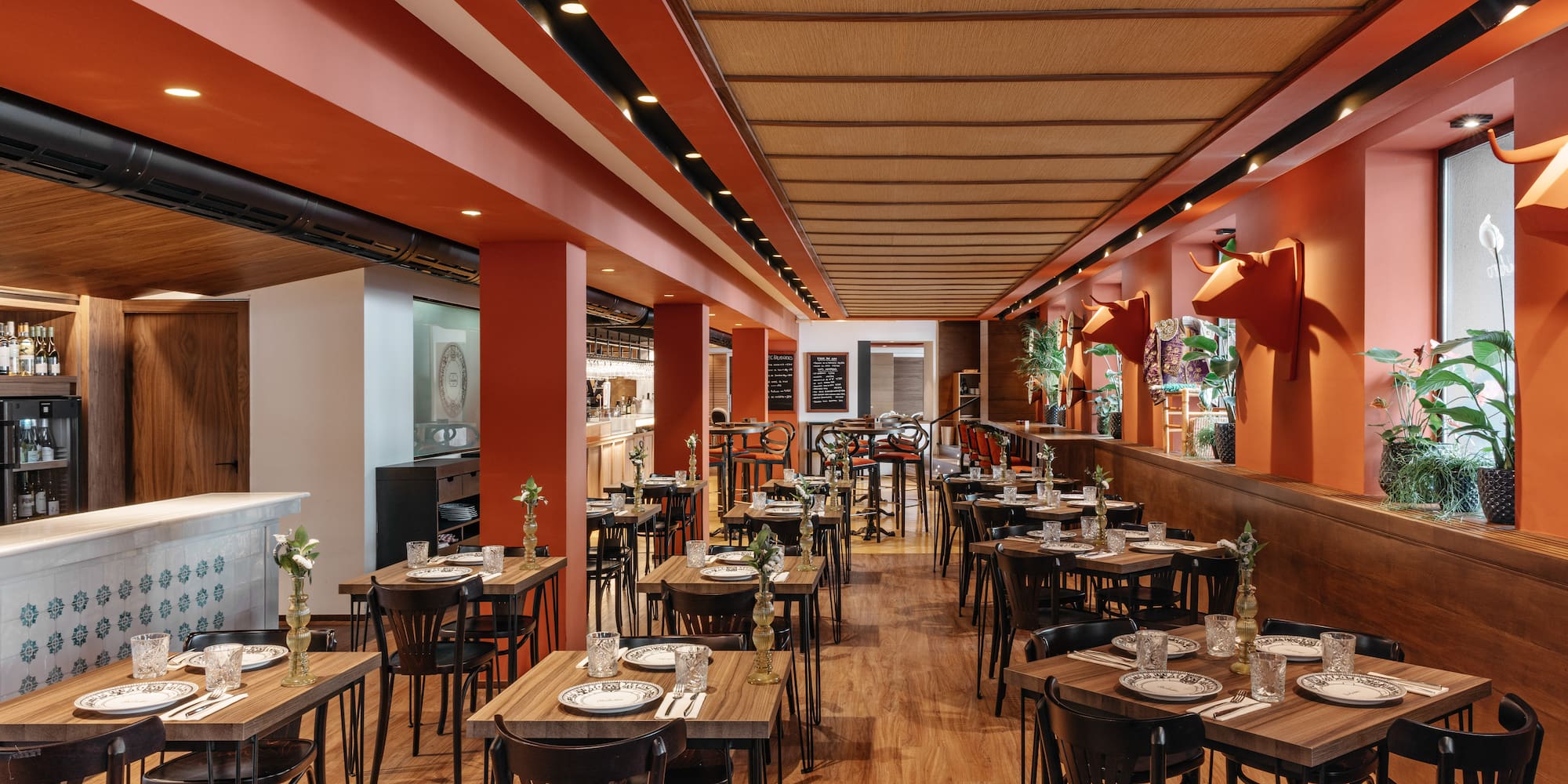 Comedor de restaurante con mesas de madera, paredes naranjas y cabezas de toro.