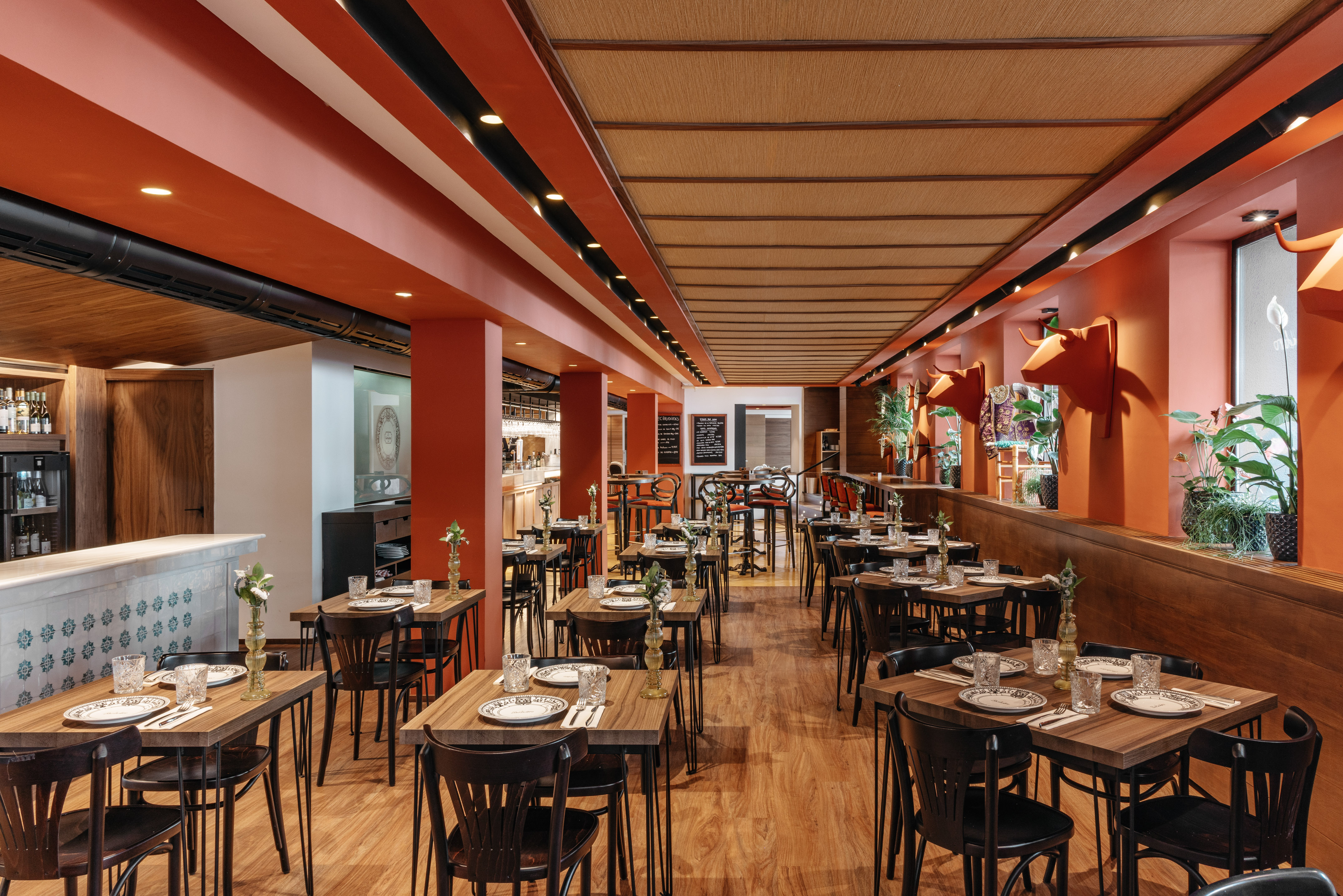 Modern restaurant interior with orange walls, wooden tables, and bull heads.