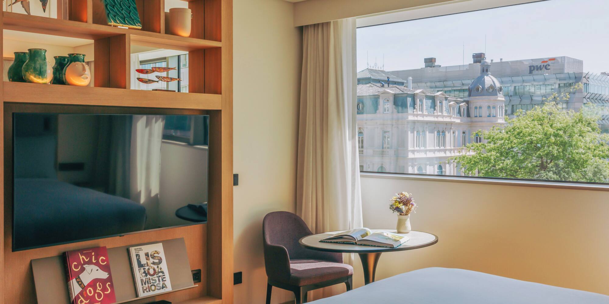 Modern hotel room with city view, large TV, and decorative wooden shelving.