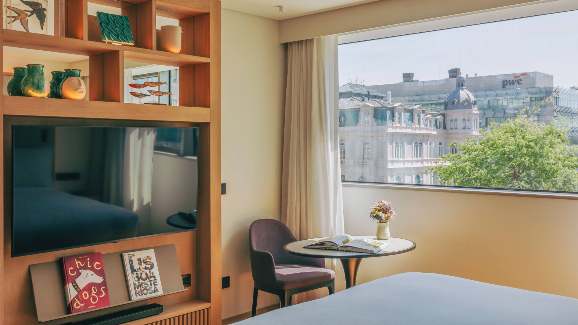 Modern hotel room with city view, large TV, and decorative wooden shelving.