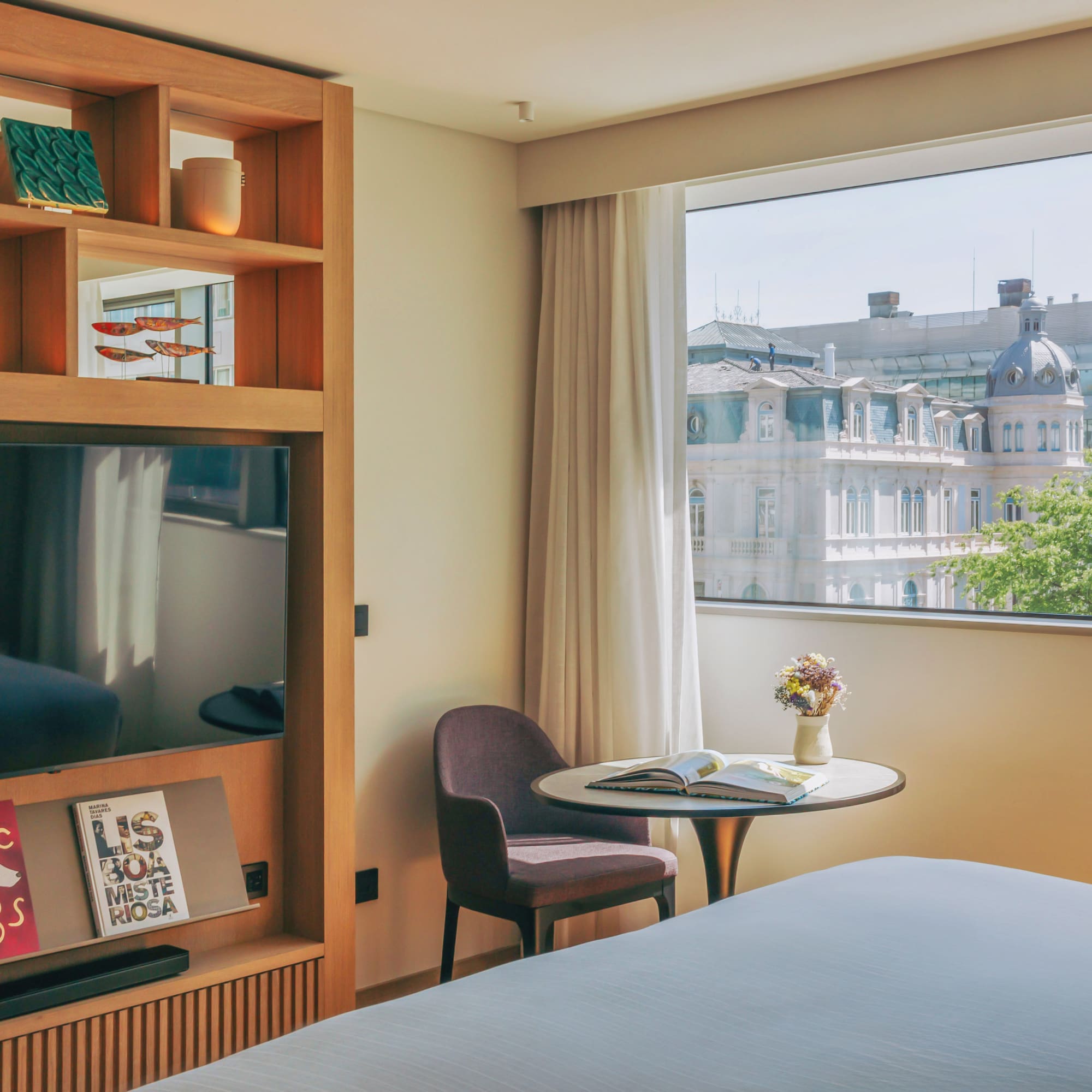 Modern hotel room with city view, large TV, and decorative wooden shelving.