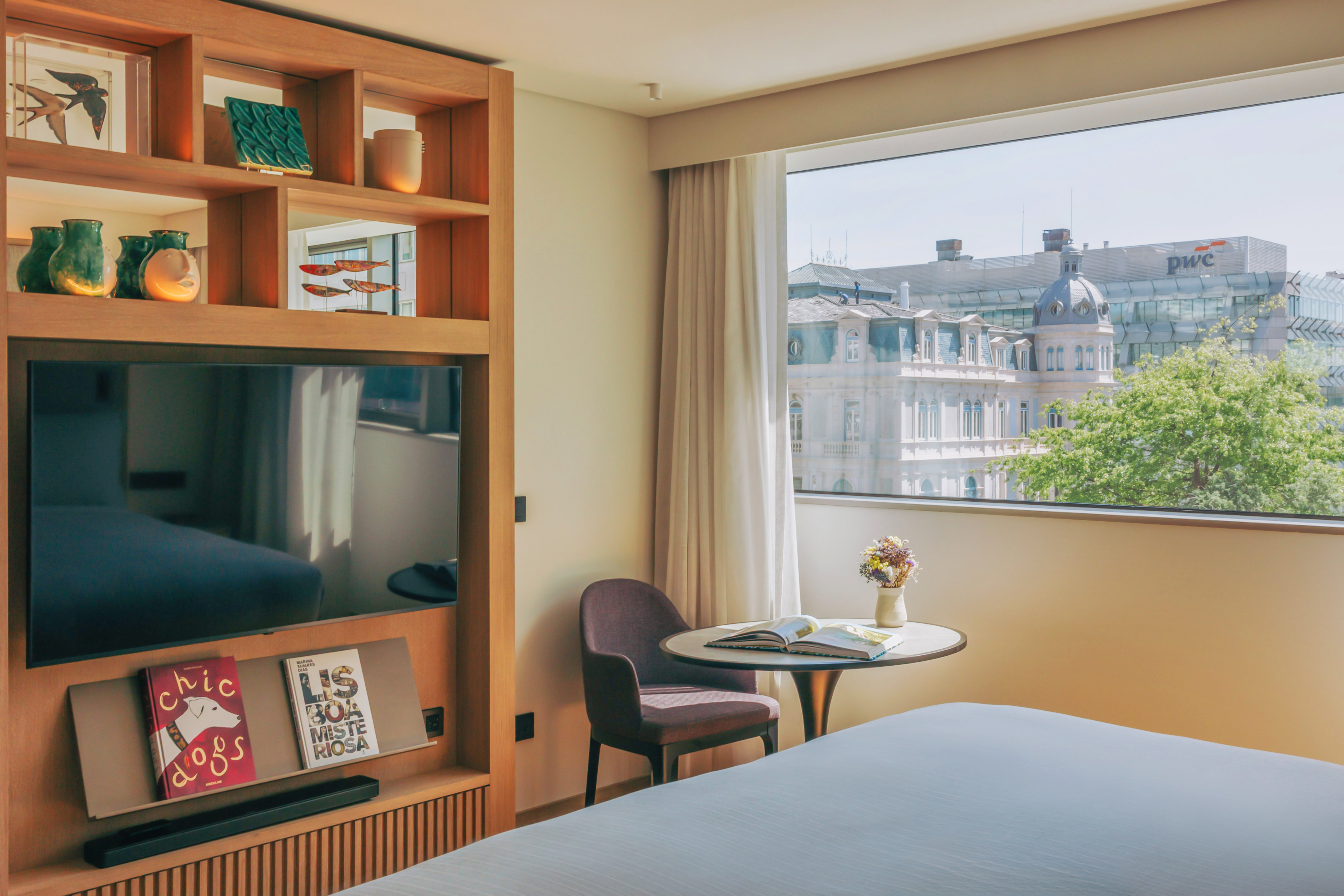 Modern hotel room with city view, large TV, and decorative wooden shelving.