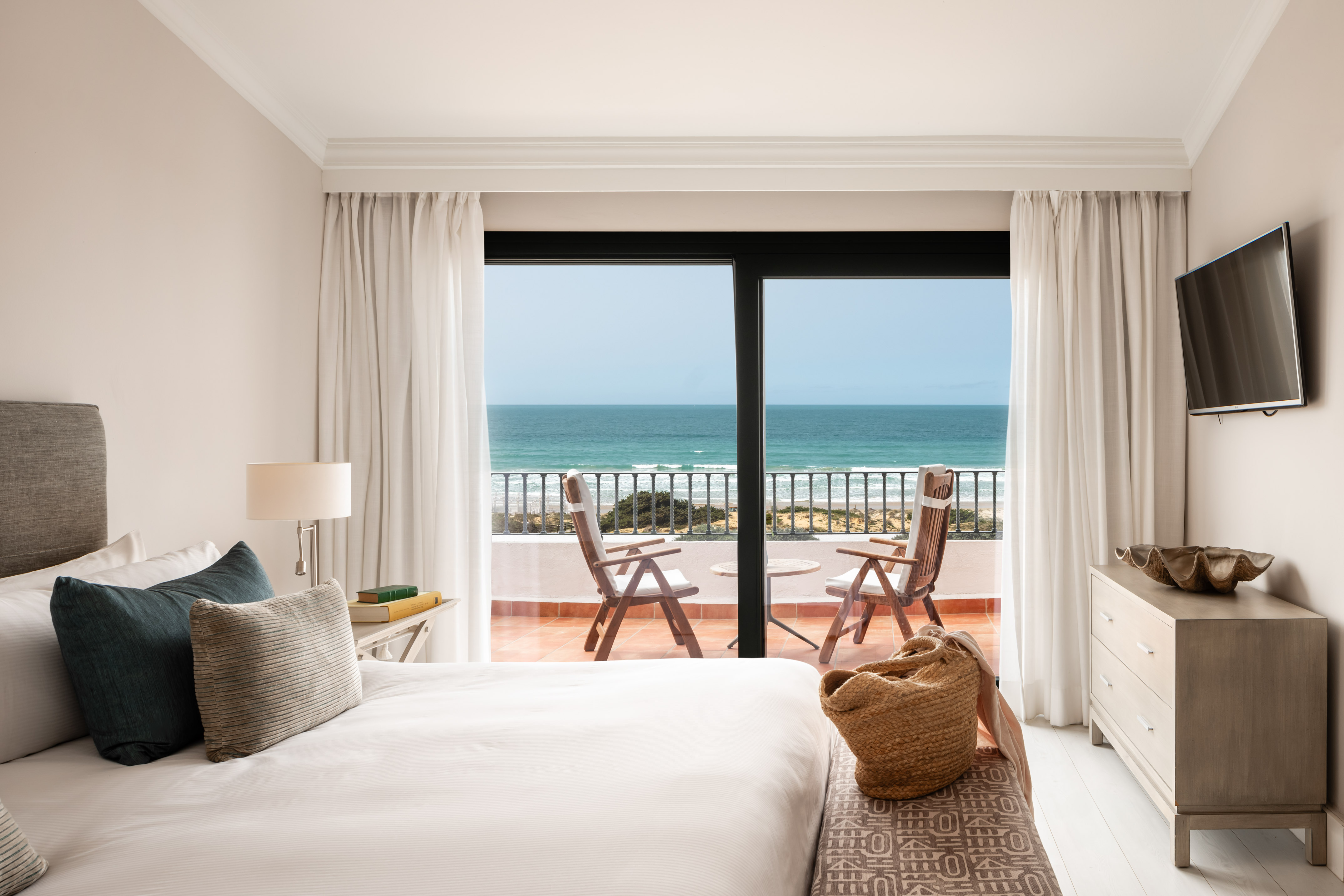 Hotel room with ocean view balcony, white bed, and coastal decor.