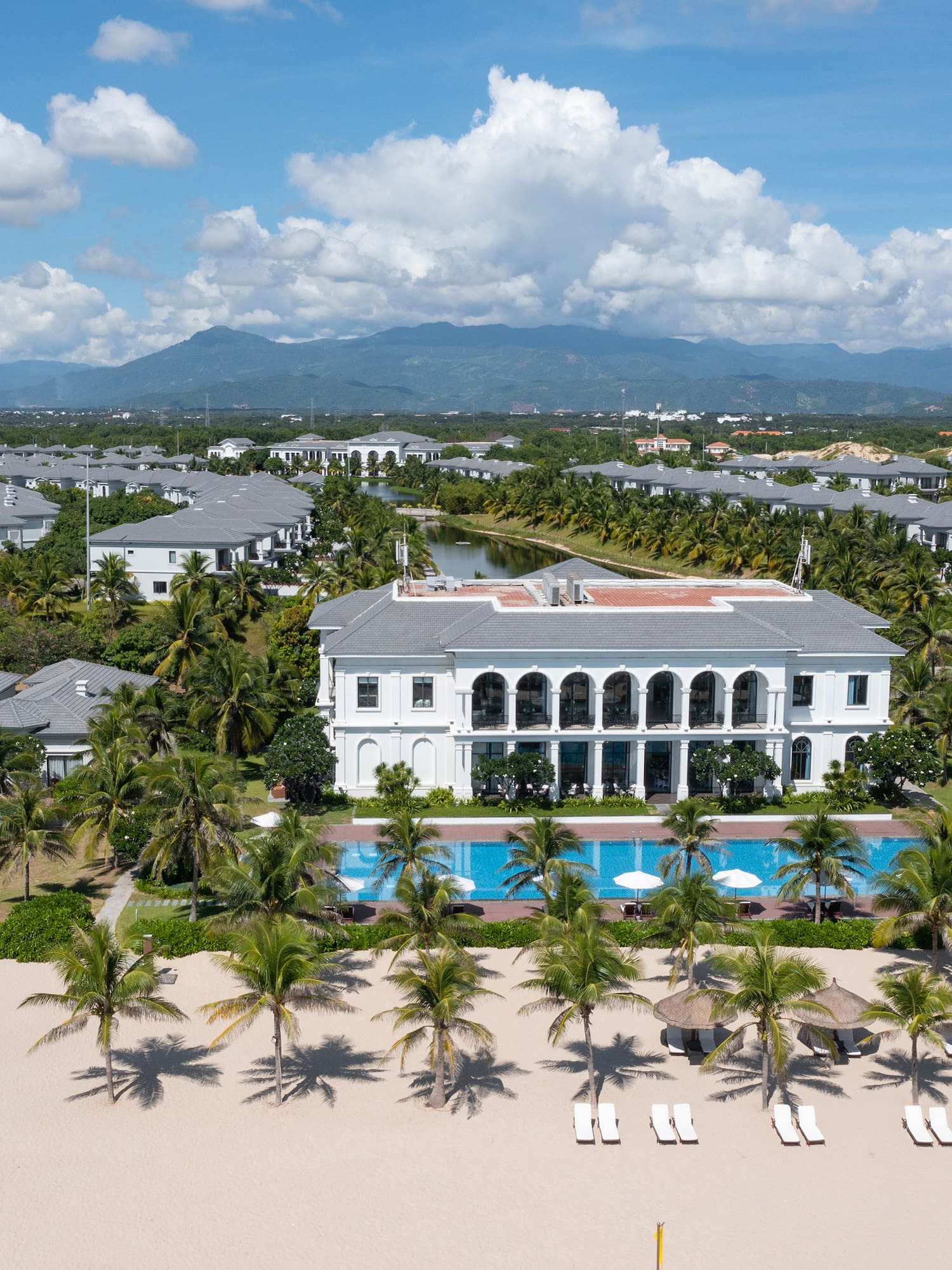 a large building with a pool and palm trees on a beach