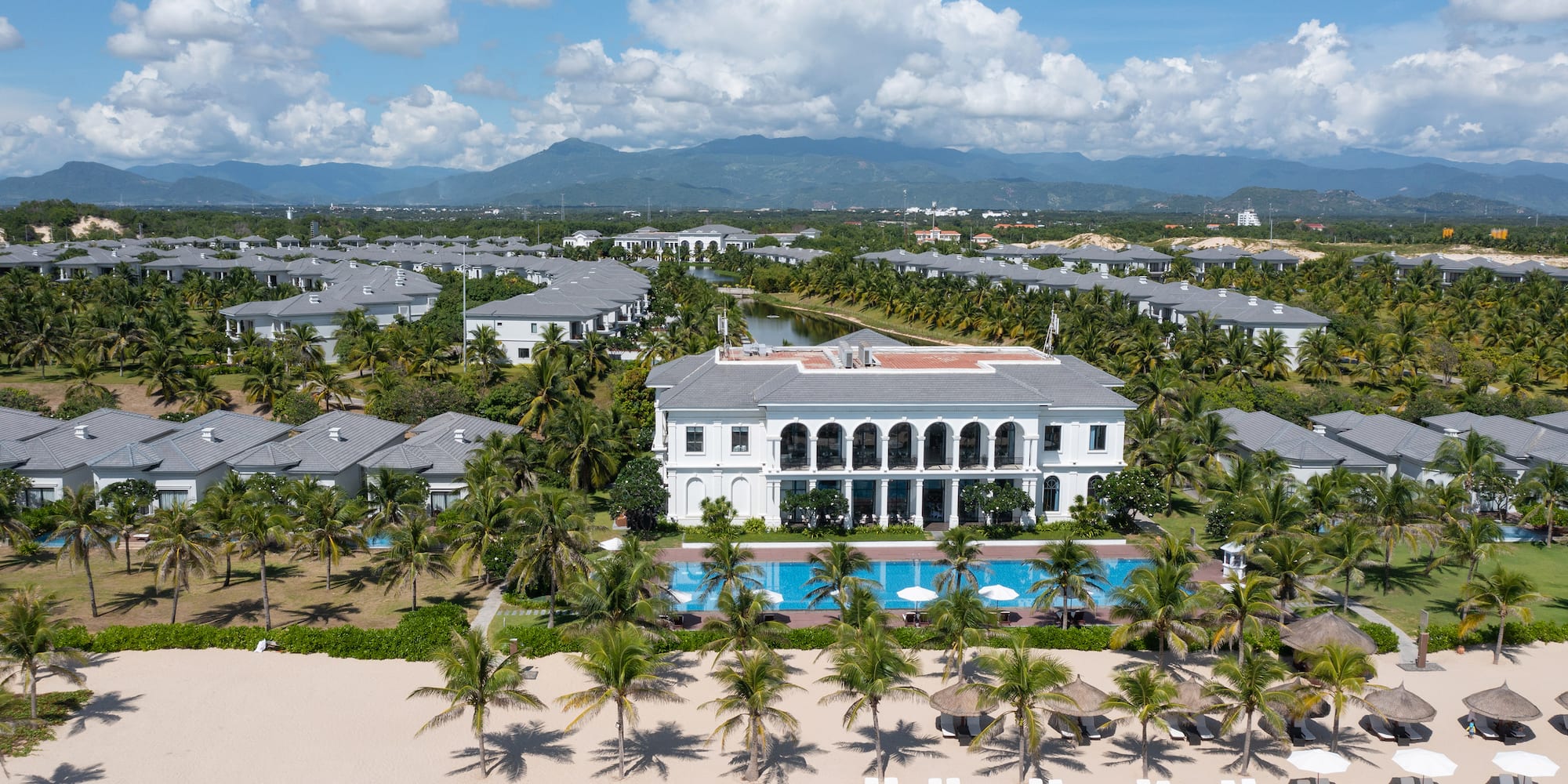 a large building with a pool and palm trees on a beach