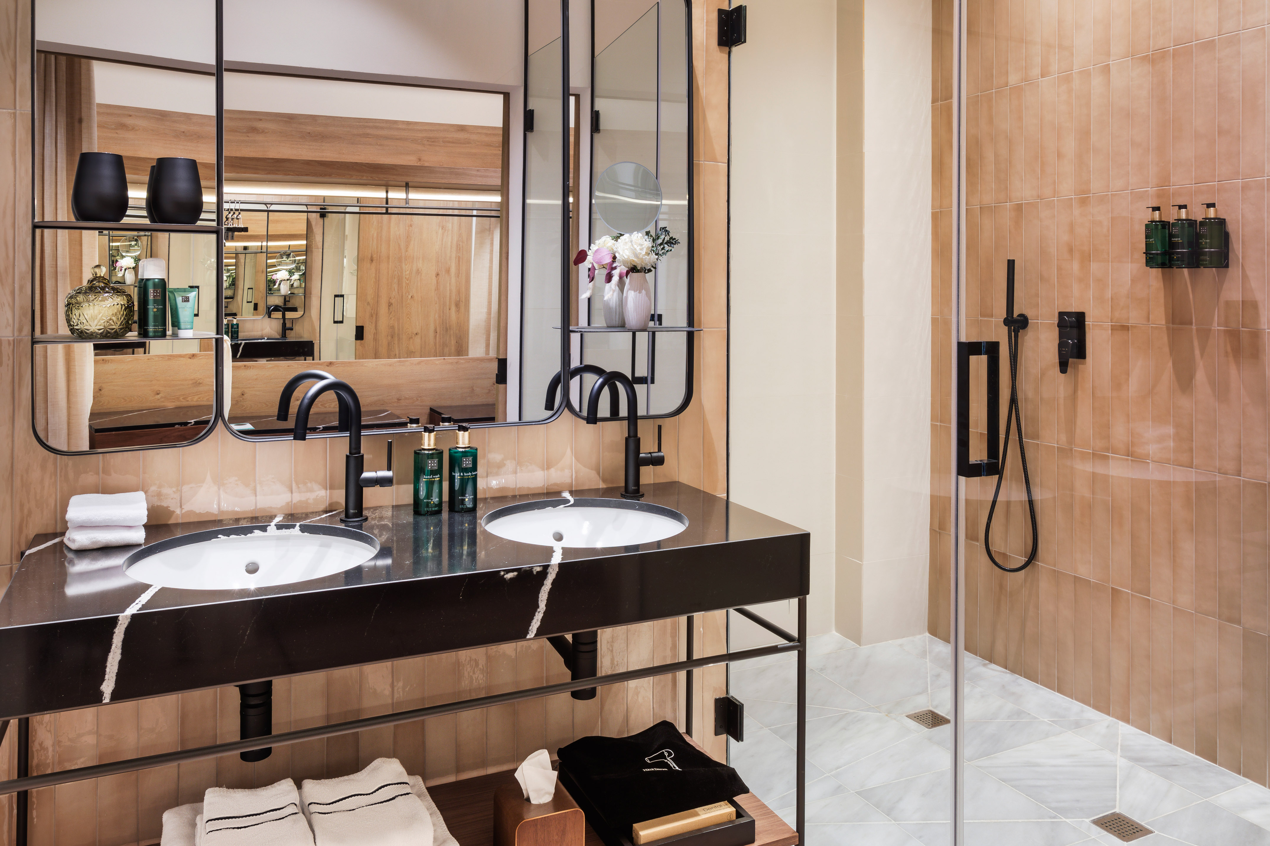 Modern bathroom with black marble double vanity, mirrors, and walk-in shower.
