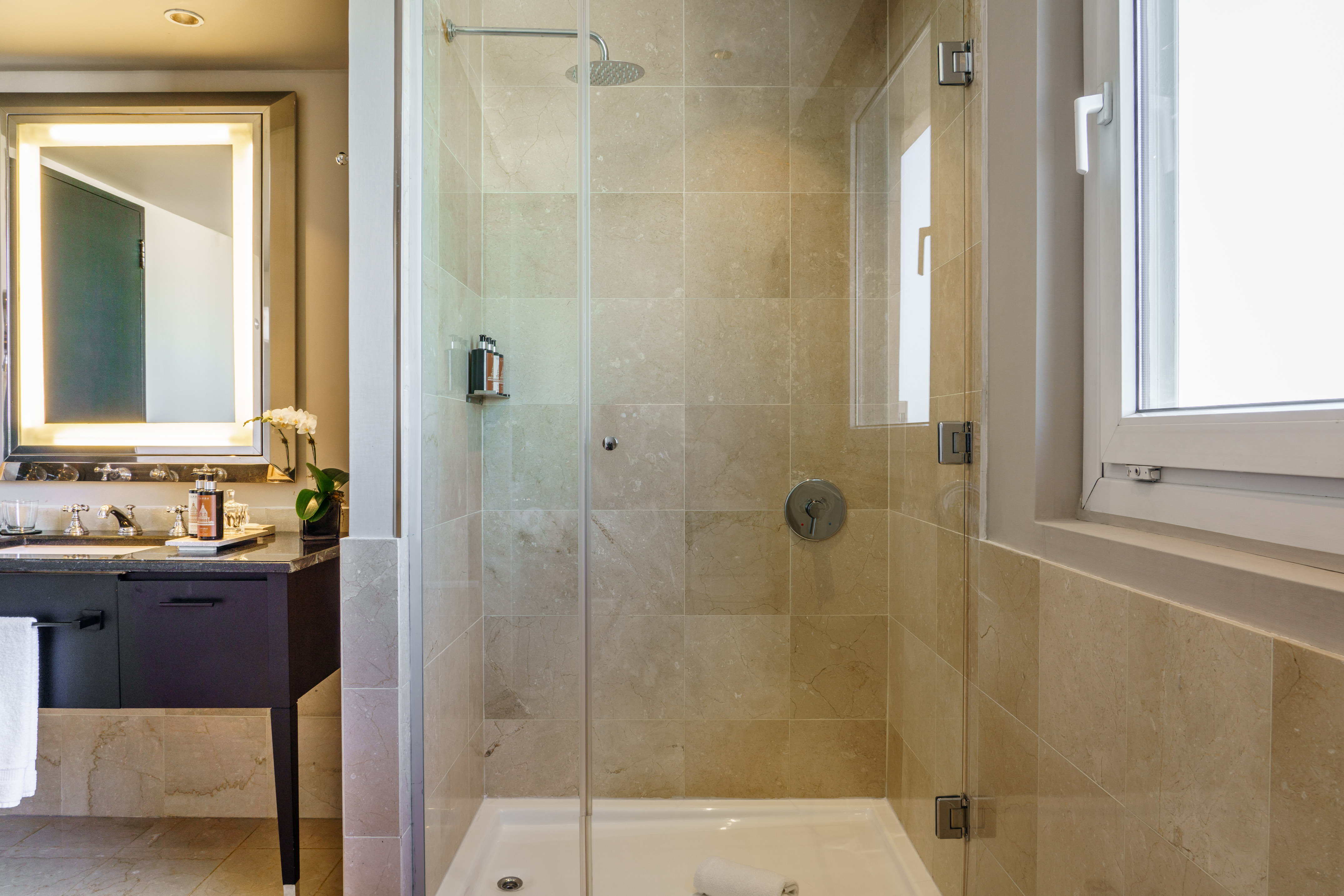 Modern bathroom with glass walk-in shower, tiled walls, vanity, and lighted mirror.