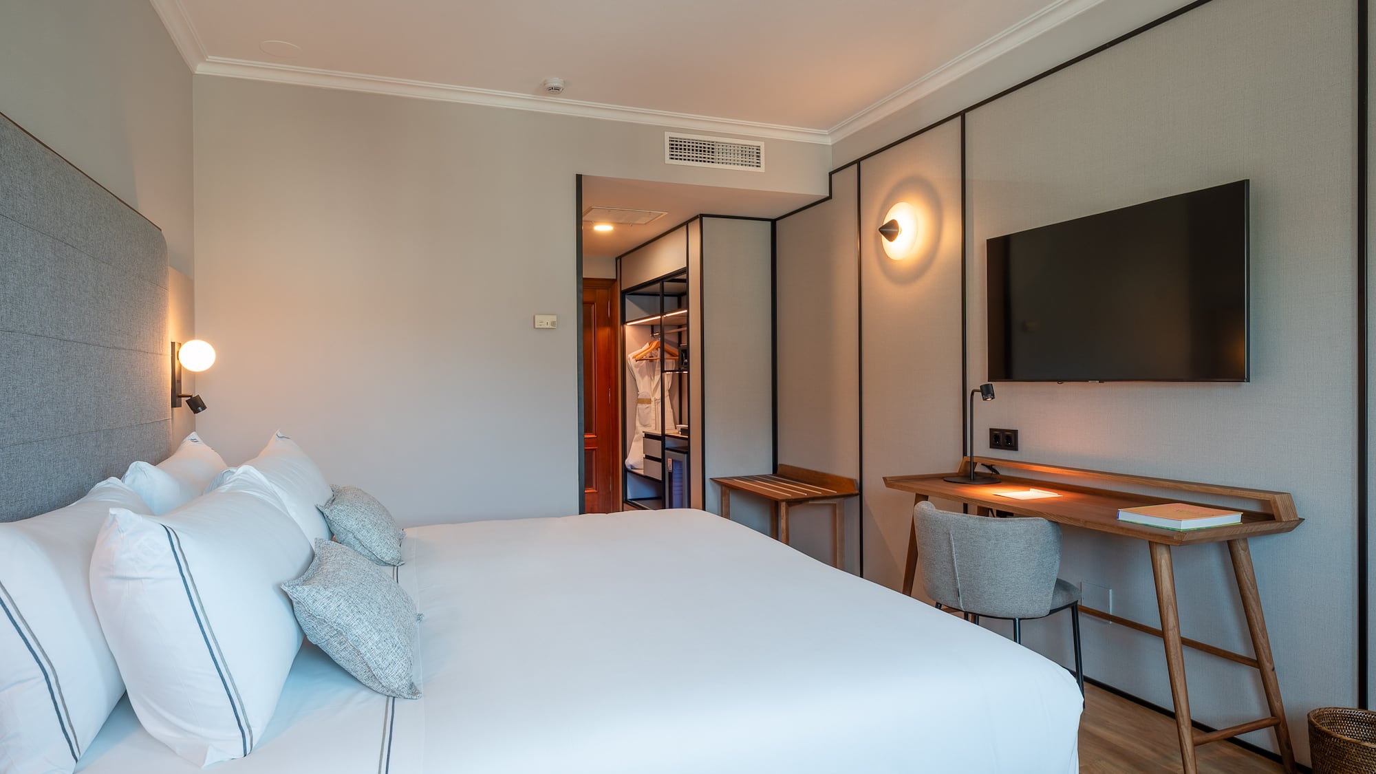 Contemporary hotel room with large bed, minimalist desk, TV, and open wardrobe.