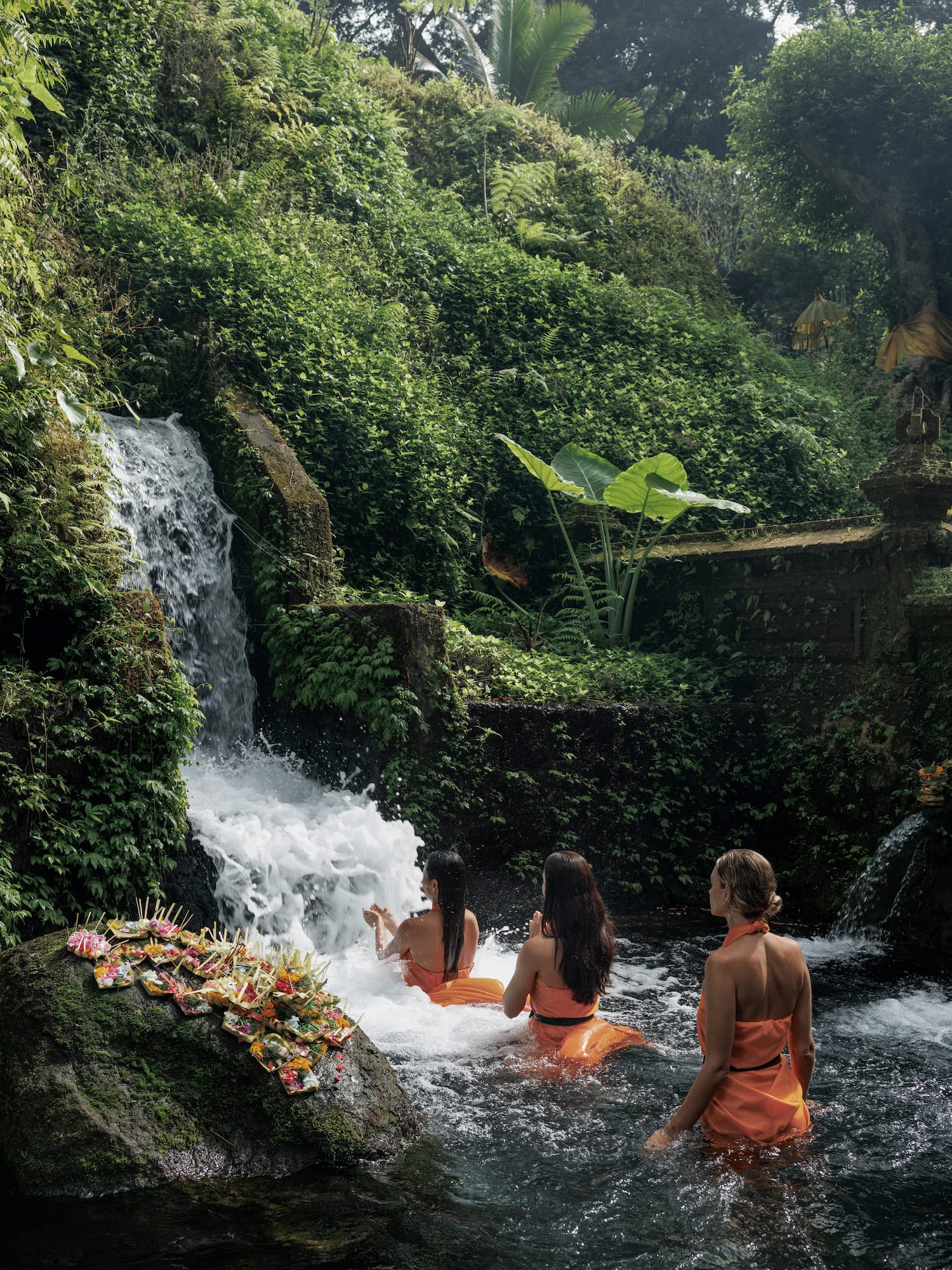 a group of women sitting in a river with a waterfall