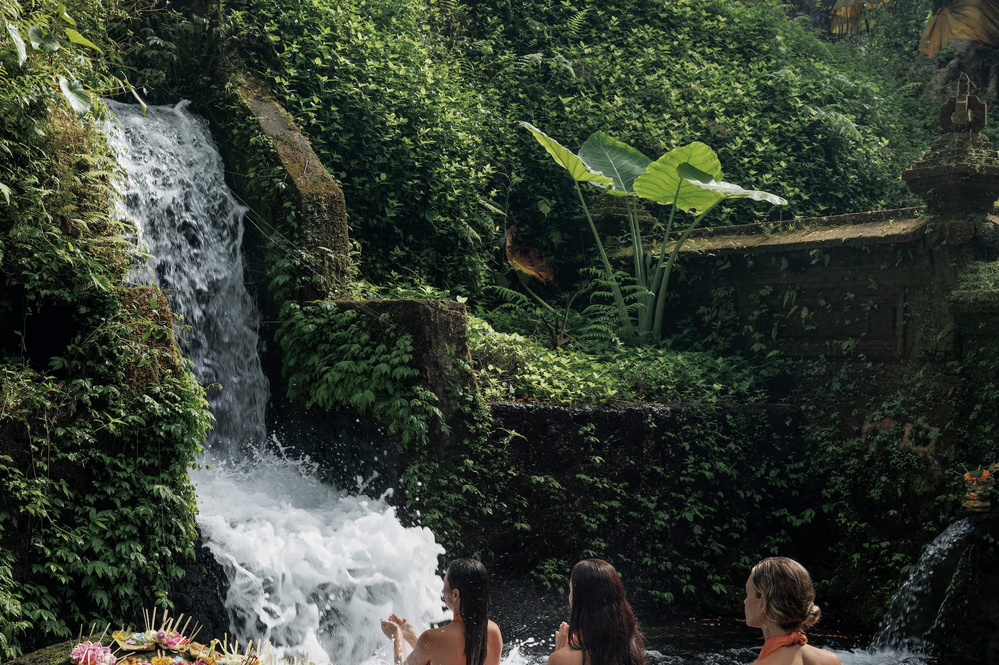 a group of women sitting in a river with a waterfall