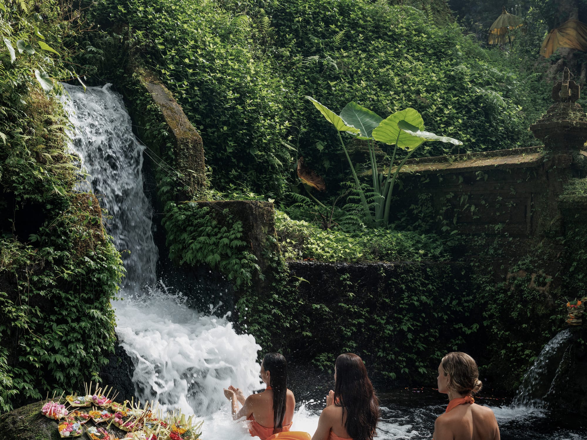 a group of women sitting in a river with a waterfall