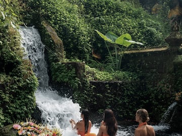 a group of women sitting in a river with a waterfall