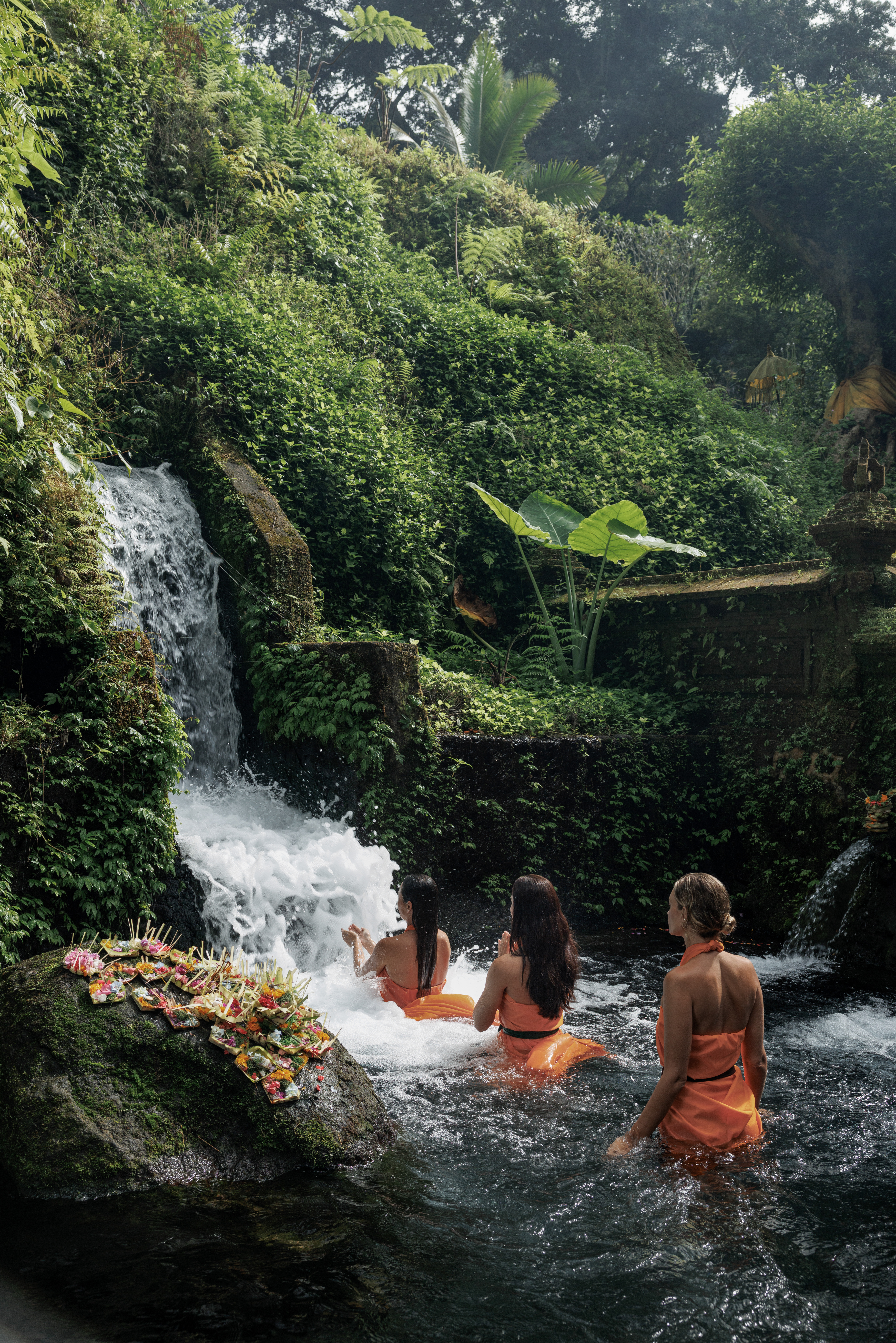 a group of women sitting in a river with a waterfall