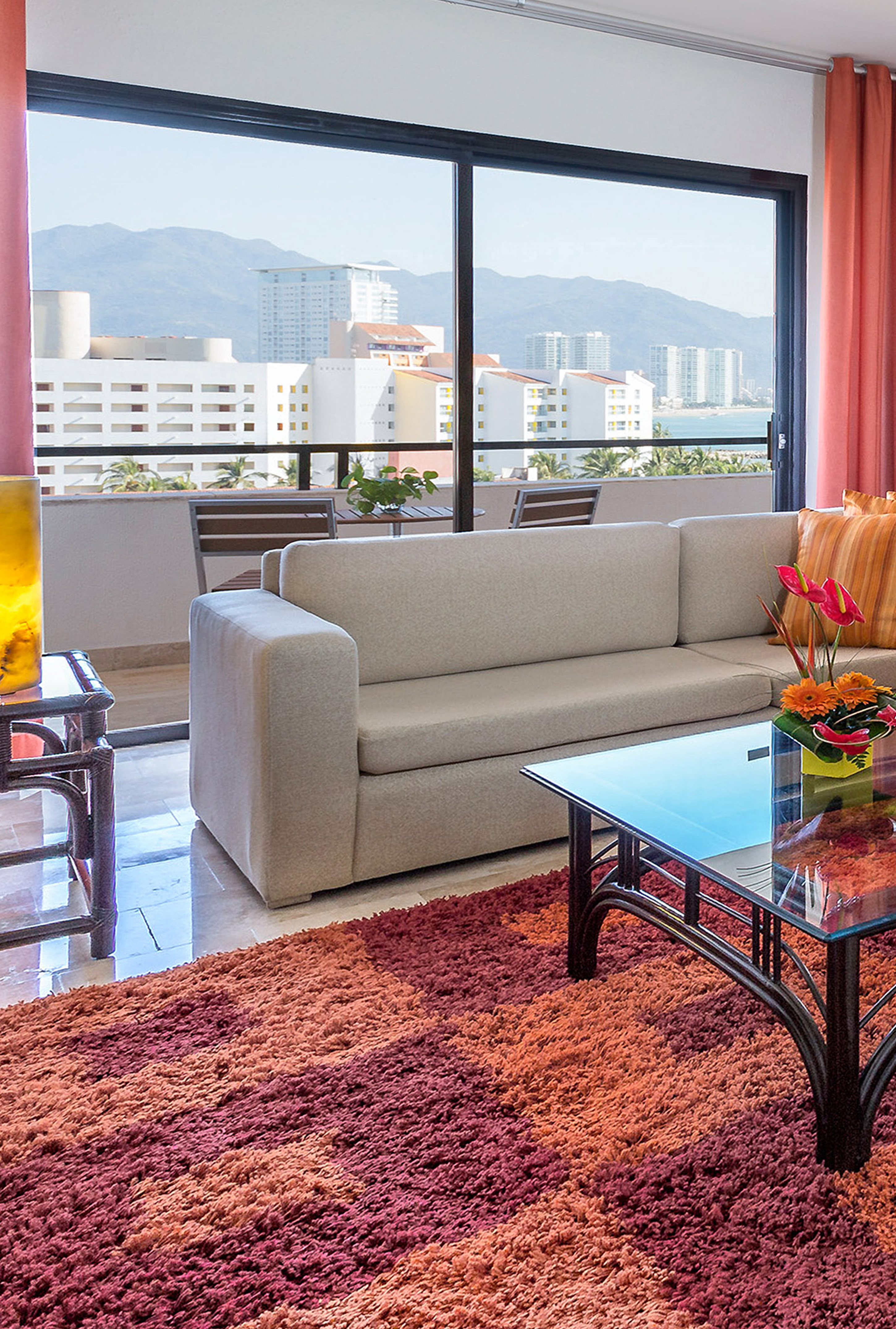 Coastal living room with modern sofa, orange rug, and city ocean view.
