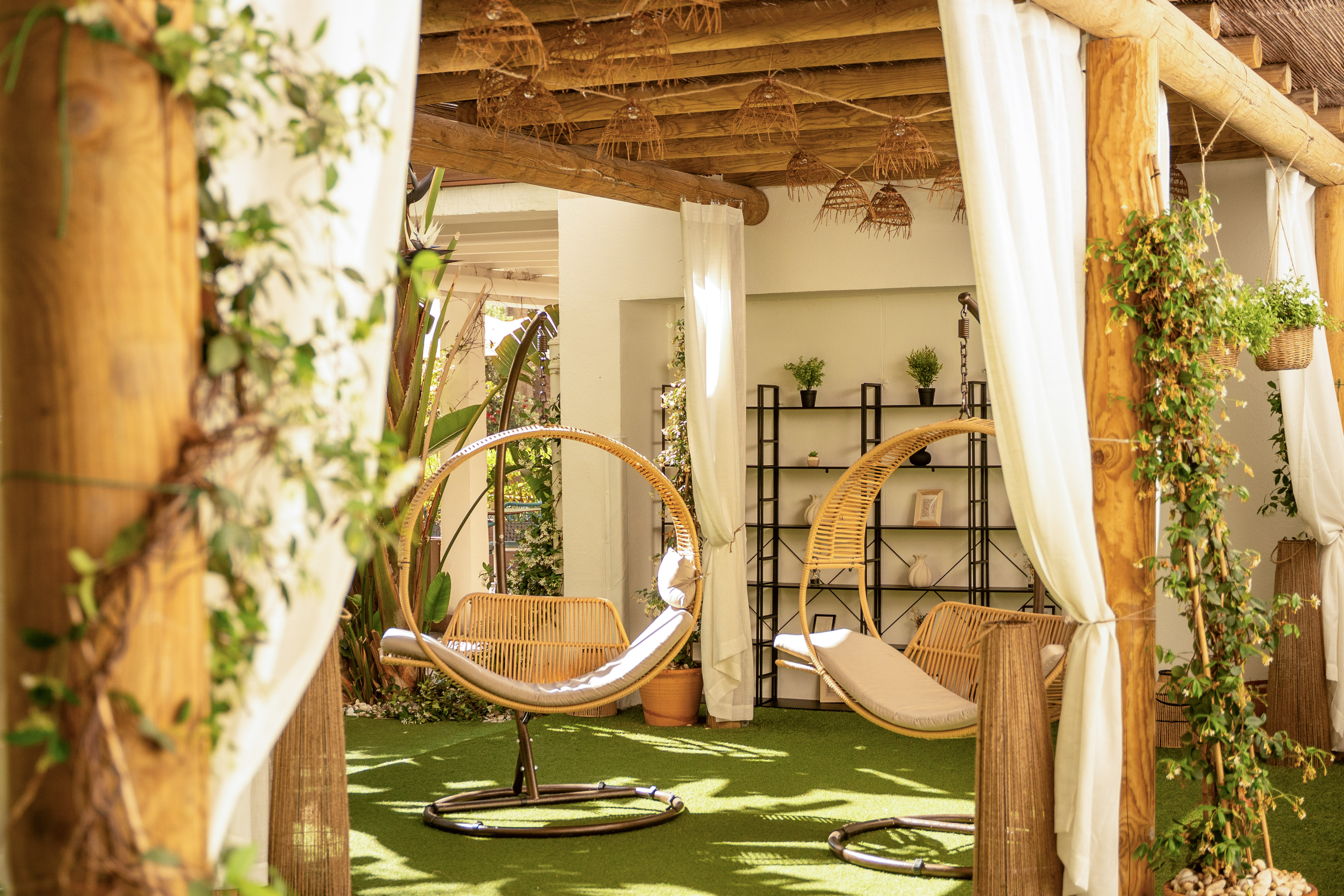 Sillas colgantes de ratán en pérgola con plantas y césped artificial para exterior.