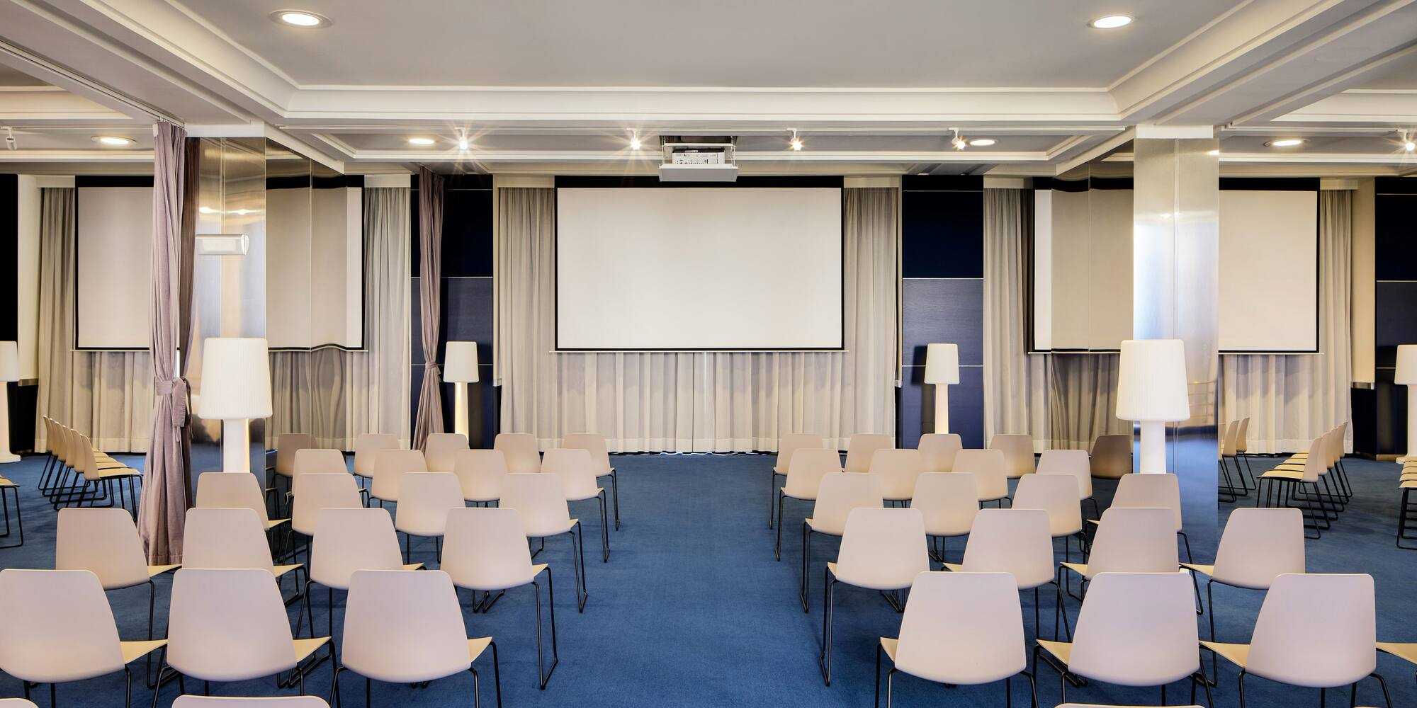 Sala de conferencias moderna con sillas claras, pantalla y proyector.