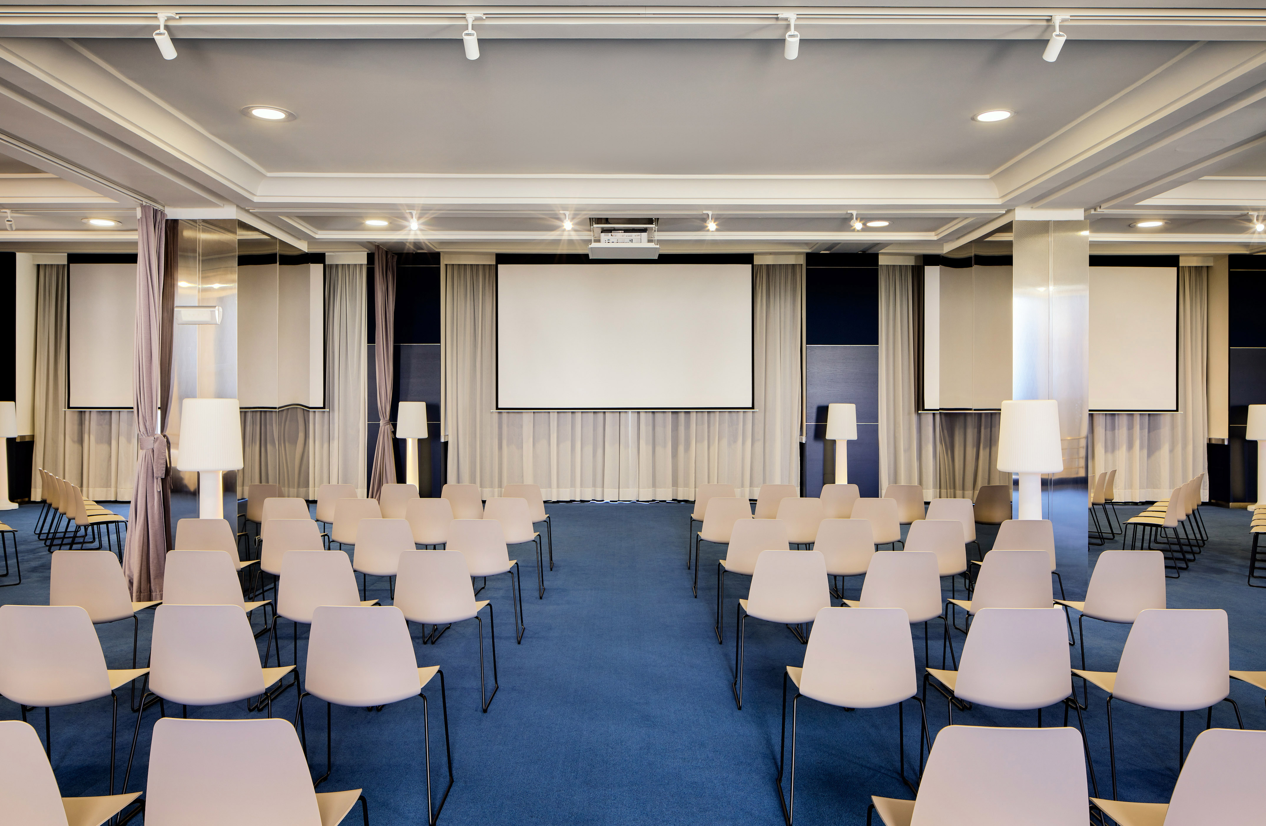 Sala de conferencias moderna con sillas claras, pantalla y proyector.