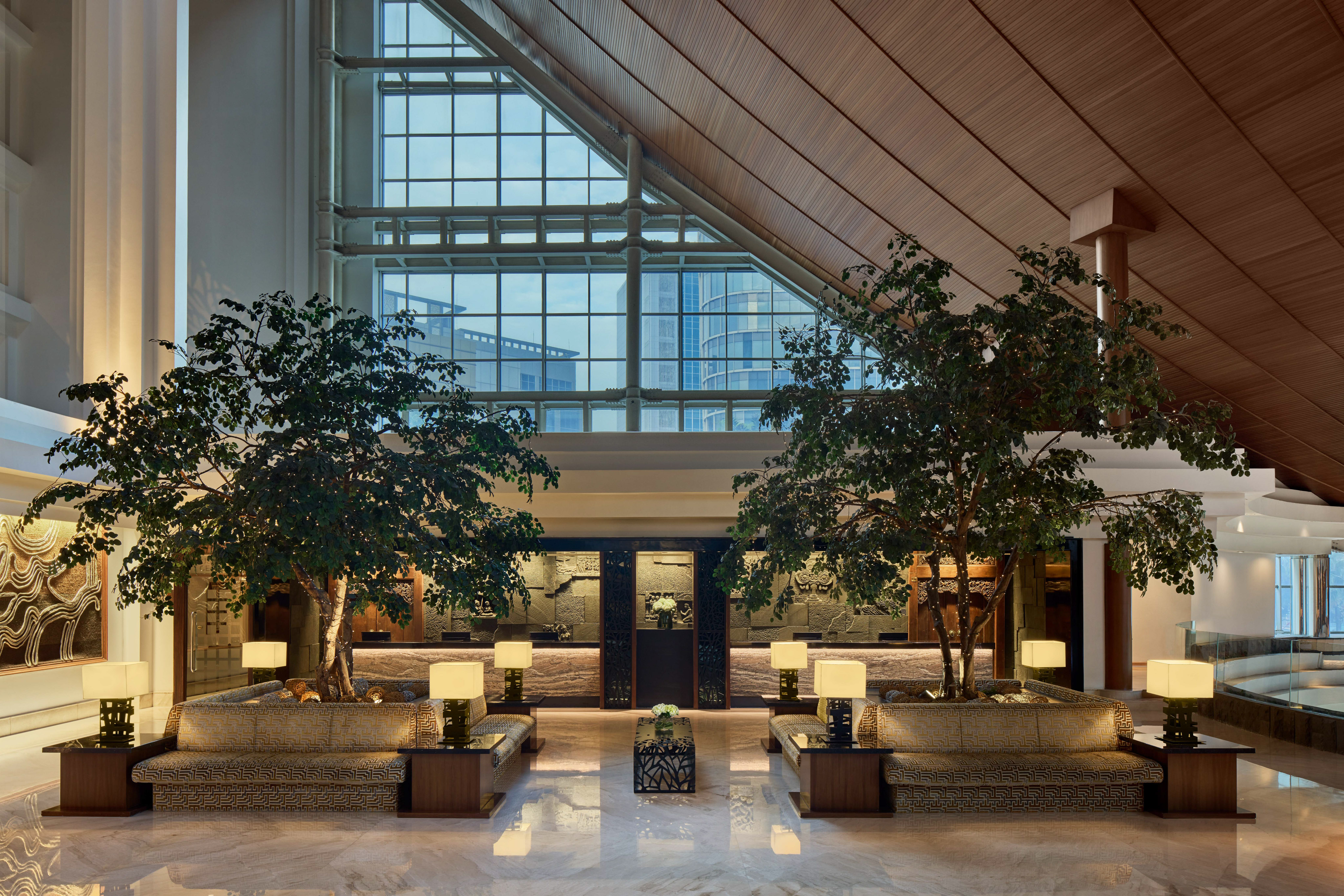 Grand hotel lobby with twin trees, elegant seating, and a striking window wall.
