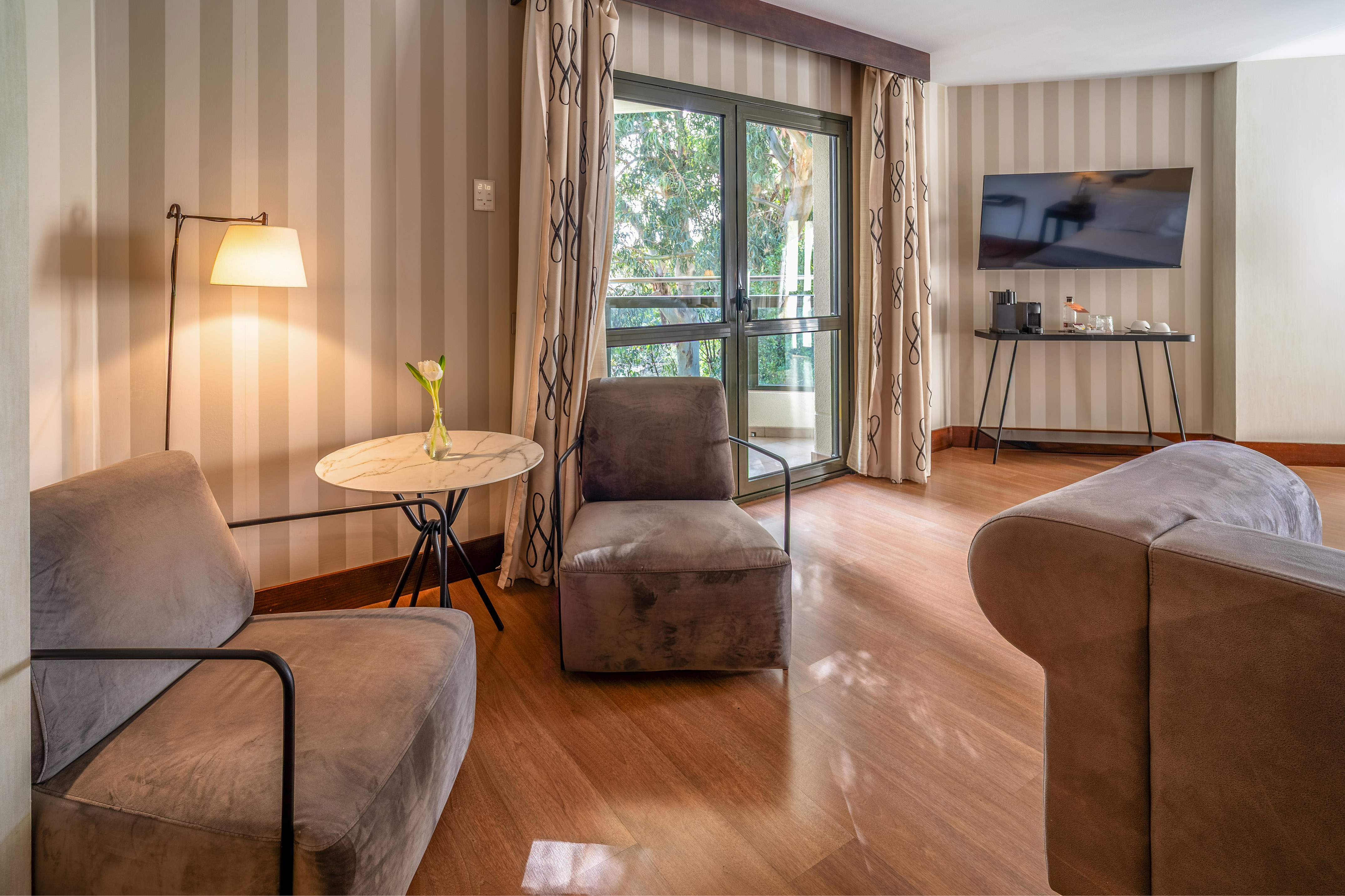 Modern hotel living area with striped walls, armchairs, wood floor, and balcony.