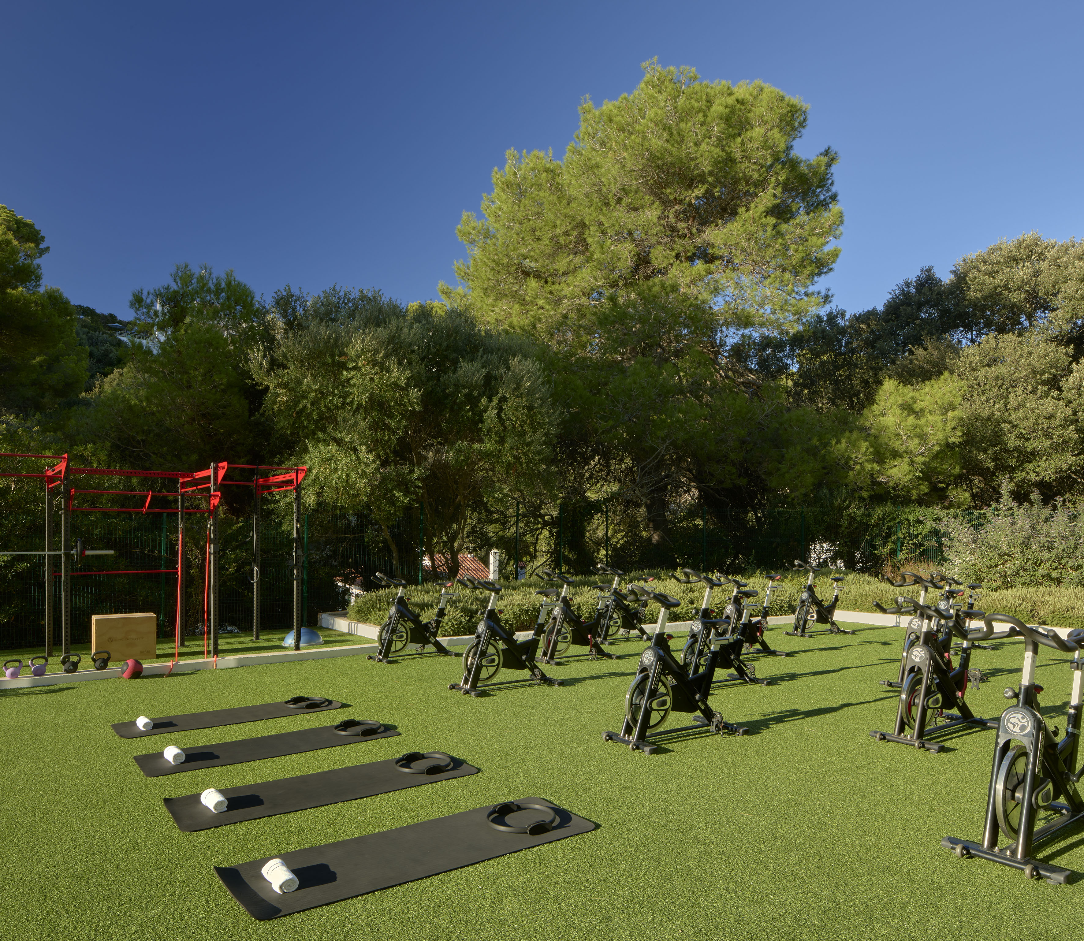 Sunny outdoor gym with spin bikes, yoga mats, and functional training rig.