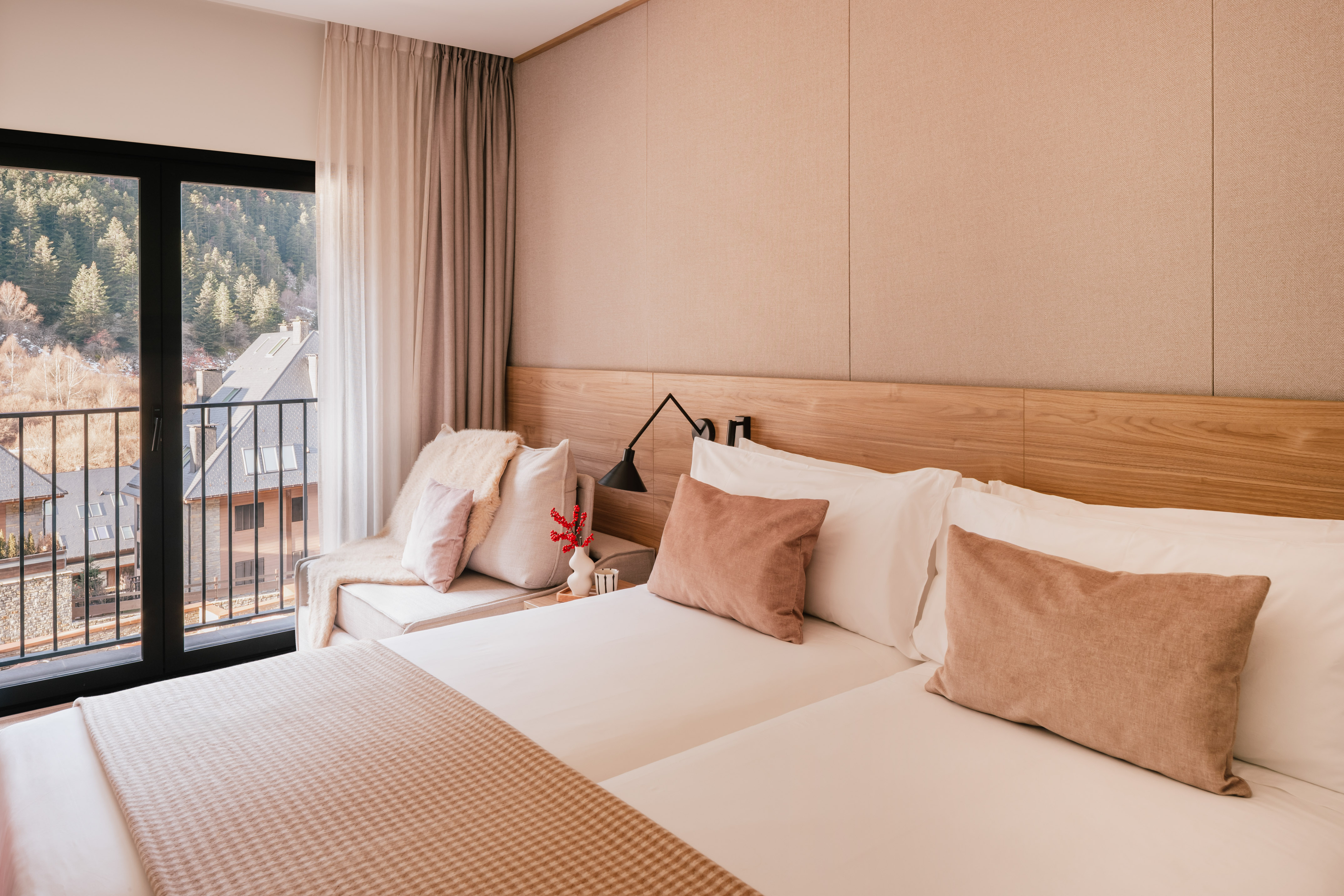 Modern hotel room with mountain view balcony and neutral wooden decor.