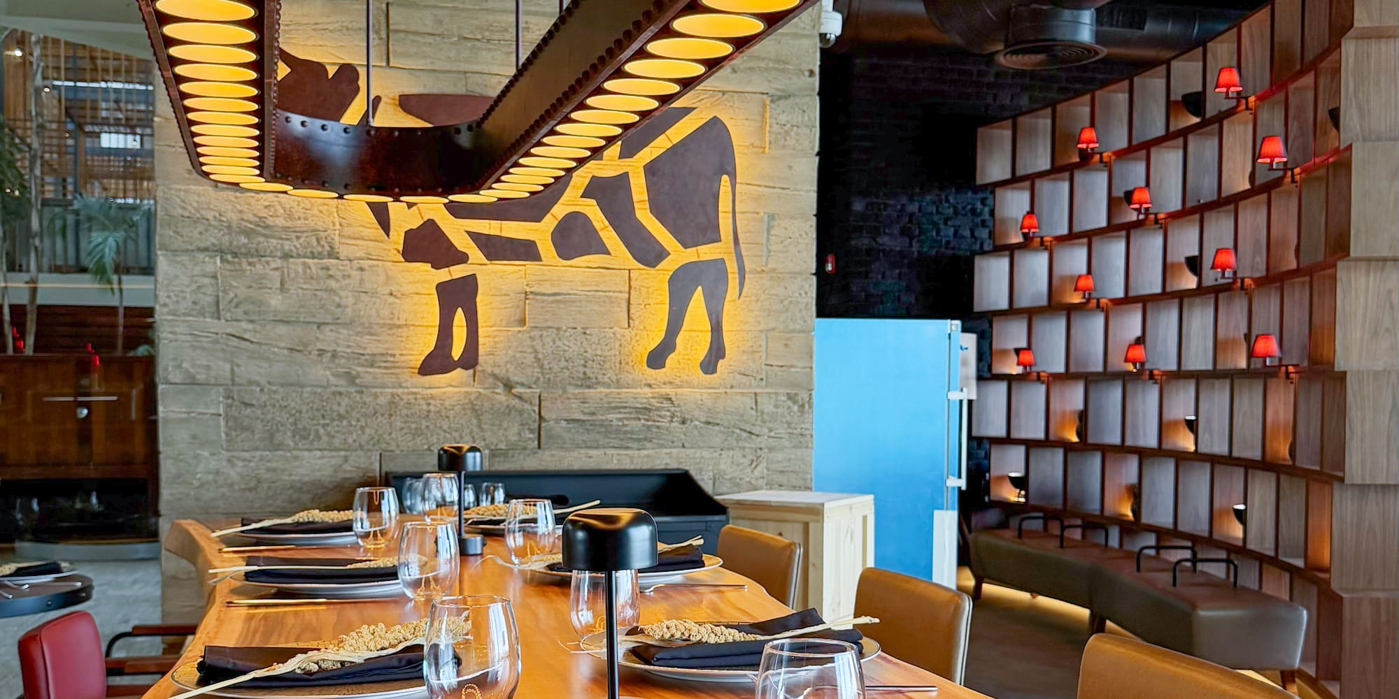 Modern restaurant dining table, industrial chandelier, glowing cow wall decor.