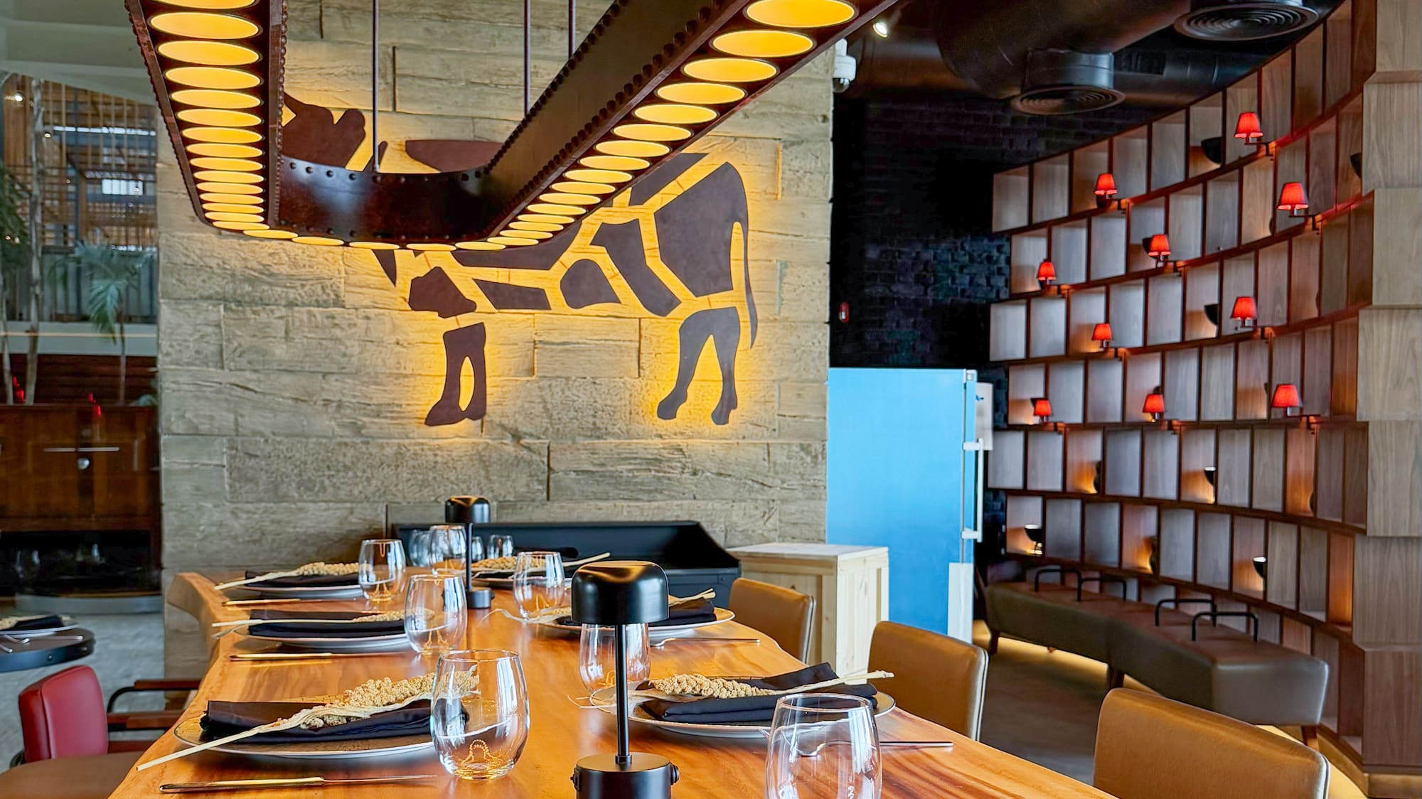 Modern restaurant dining table, industrial chandelier, glowing cow wall decor.
