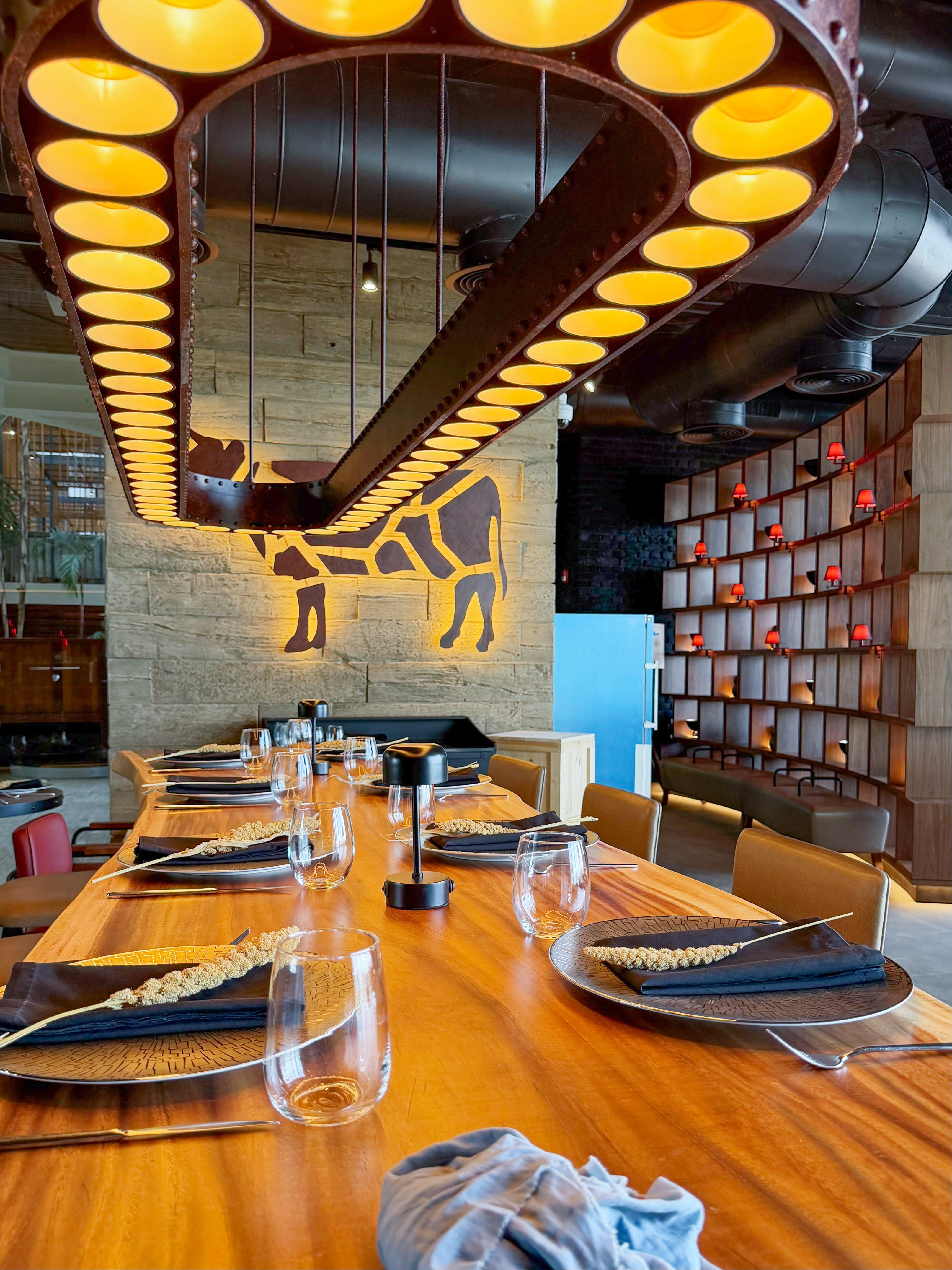 Modern restaurant dining table, industrial chandelier, glowing cow wall decor.