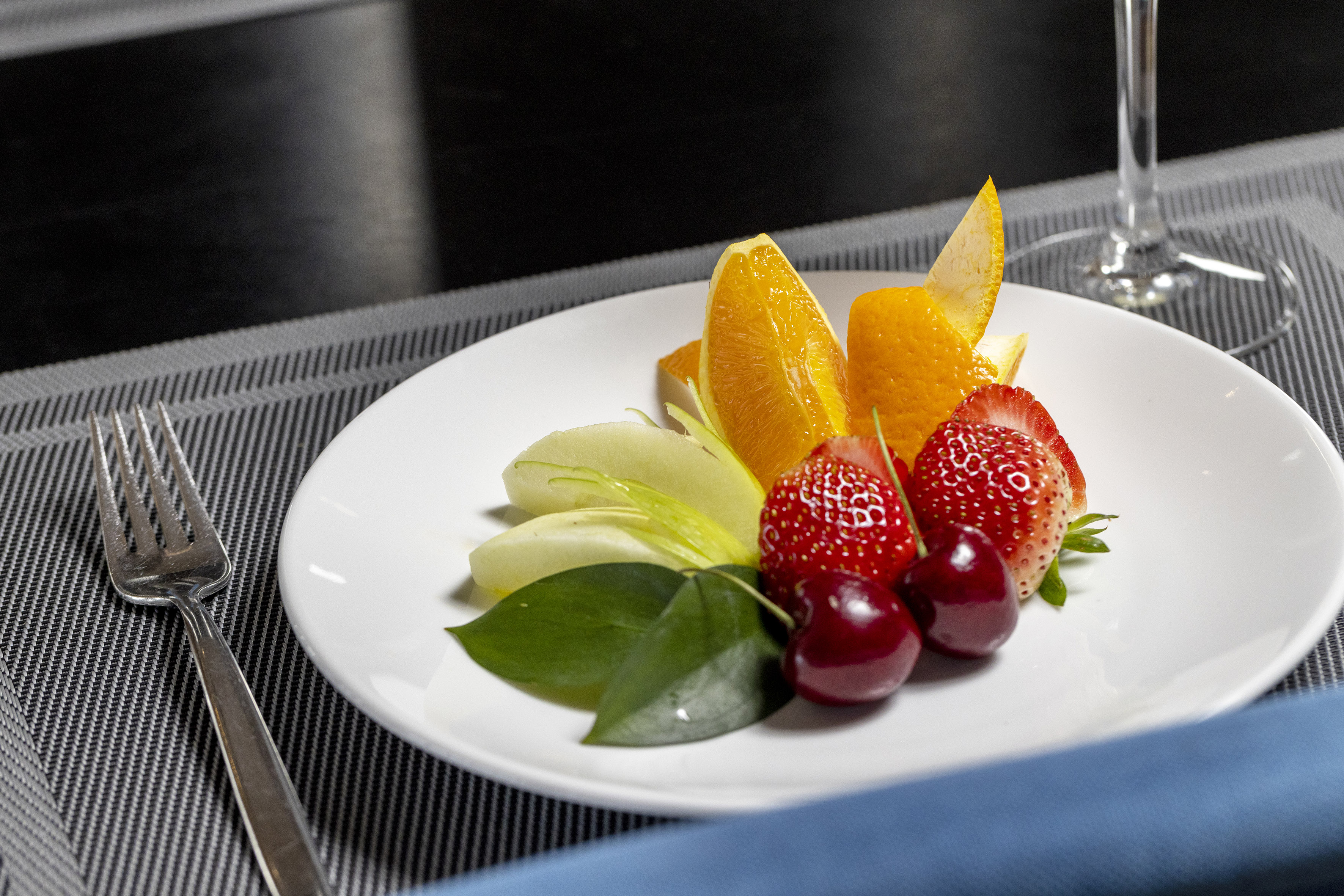 Fresh fruit plate with orange, apple, strawberries, cherries, and green garnish.