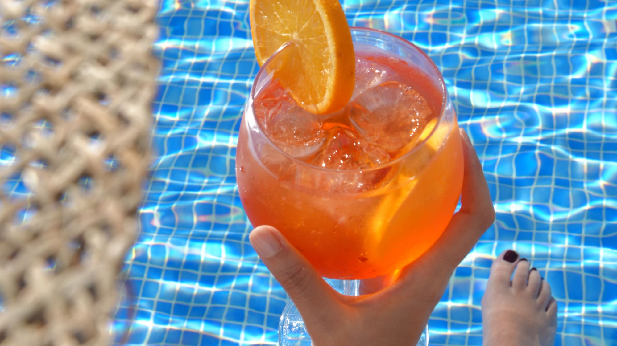 a person holding a drink in front of a pool