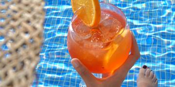 a person holding a drink in front of a pool