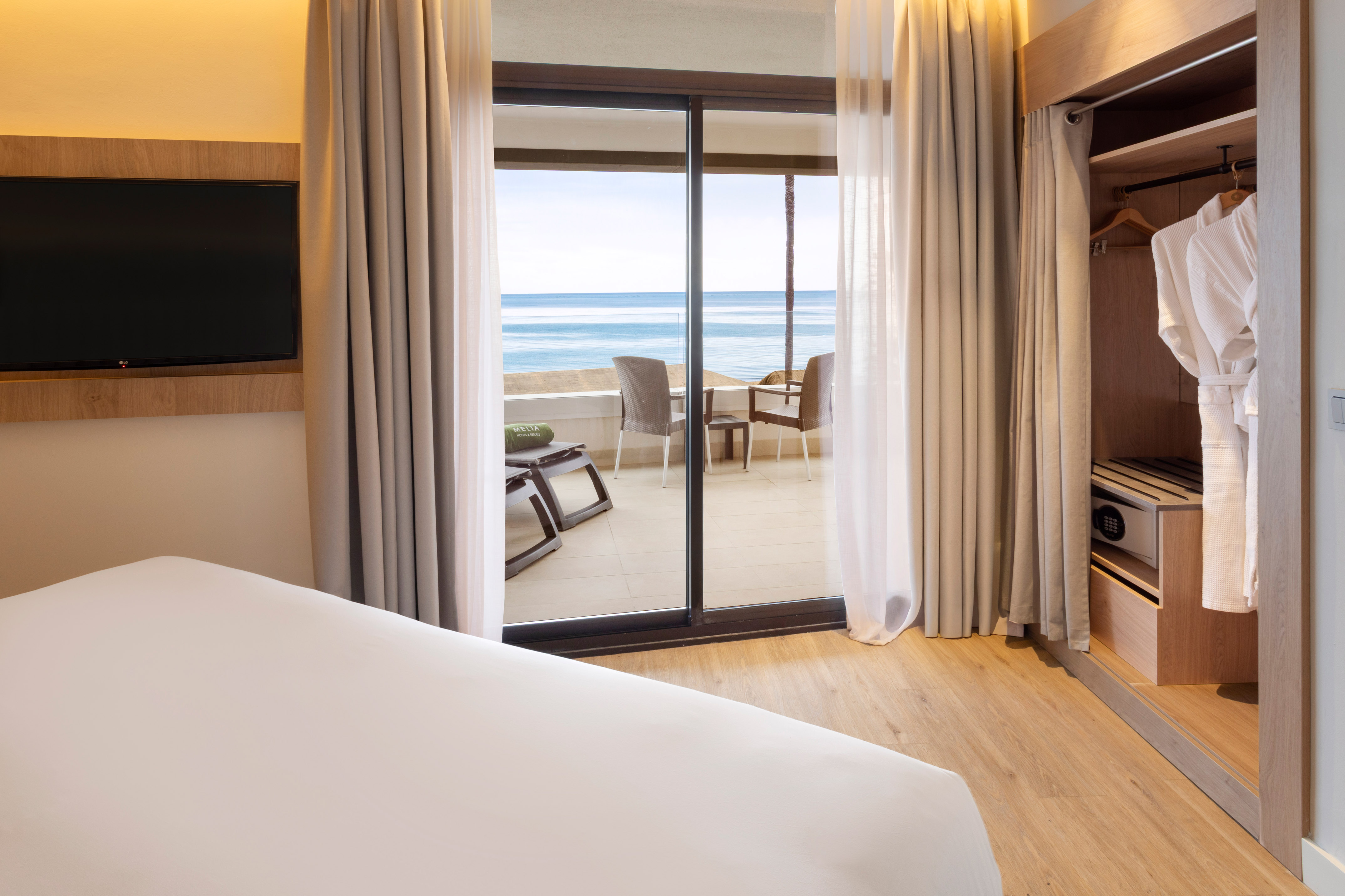 Modern hotel bedroom with ocean view balcony, TV, and open closet.