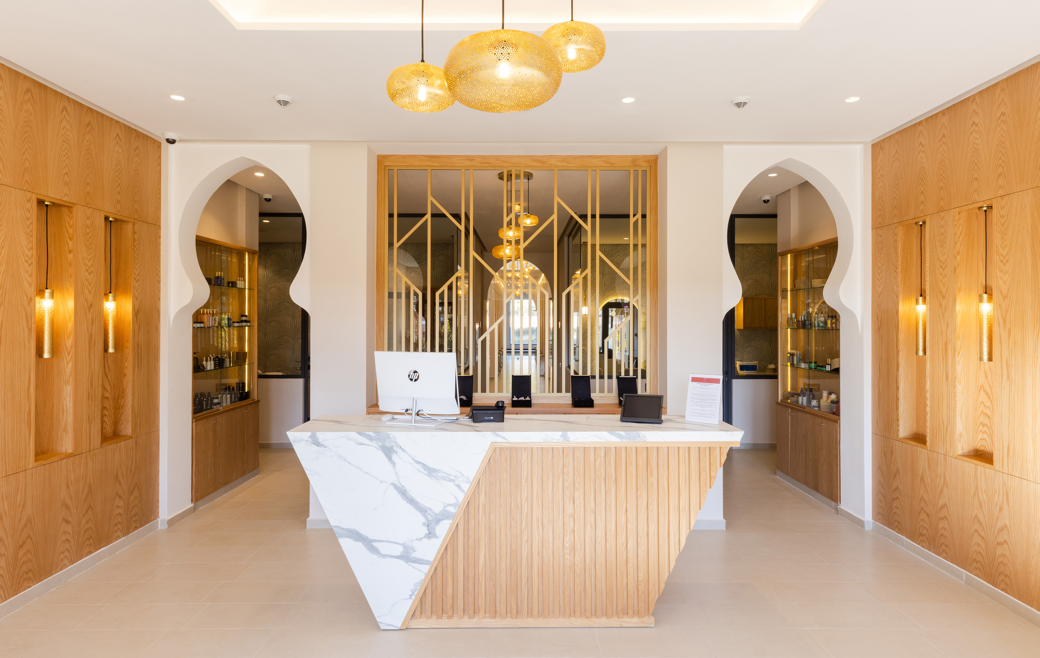Modern reception desk with marble and wood, Moroccan arches, golden pendant lights.