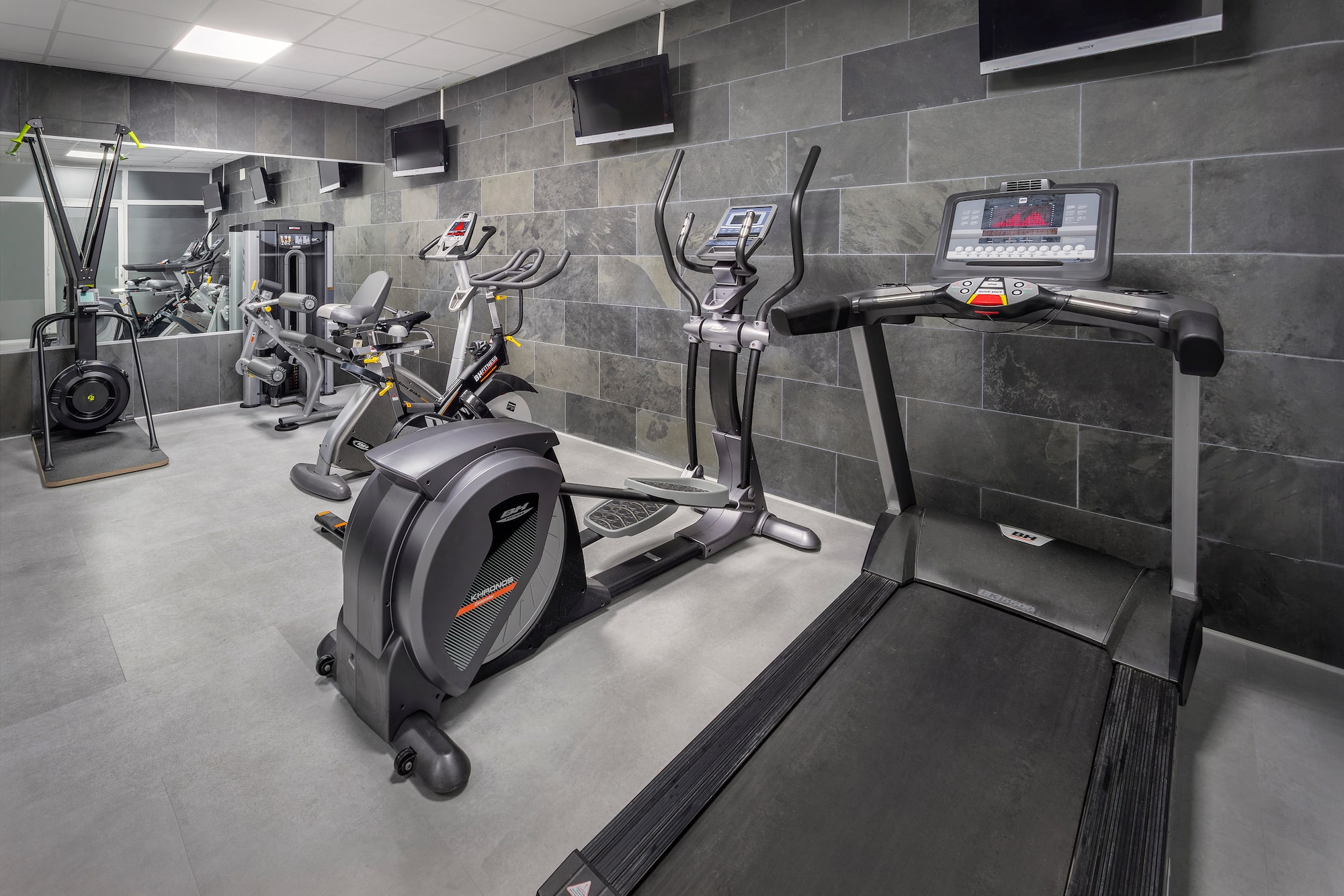 Gimnasio moderno con cinta de correr, elíptica, bicicleta y máquinas.