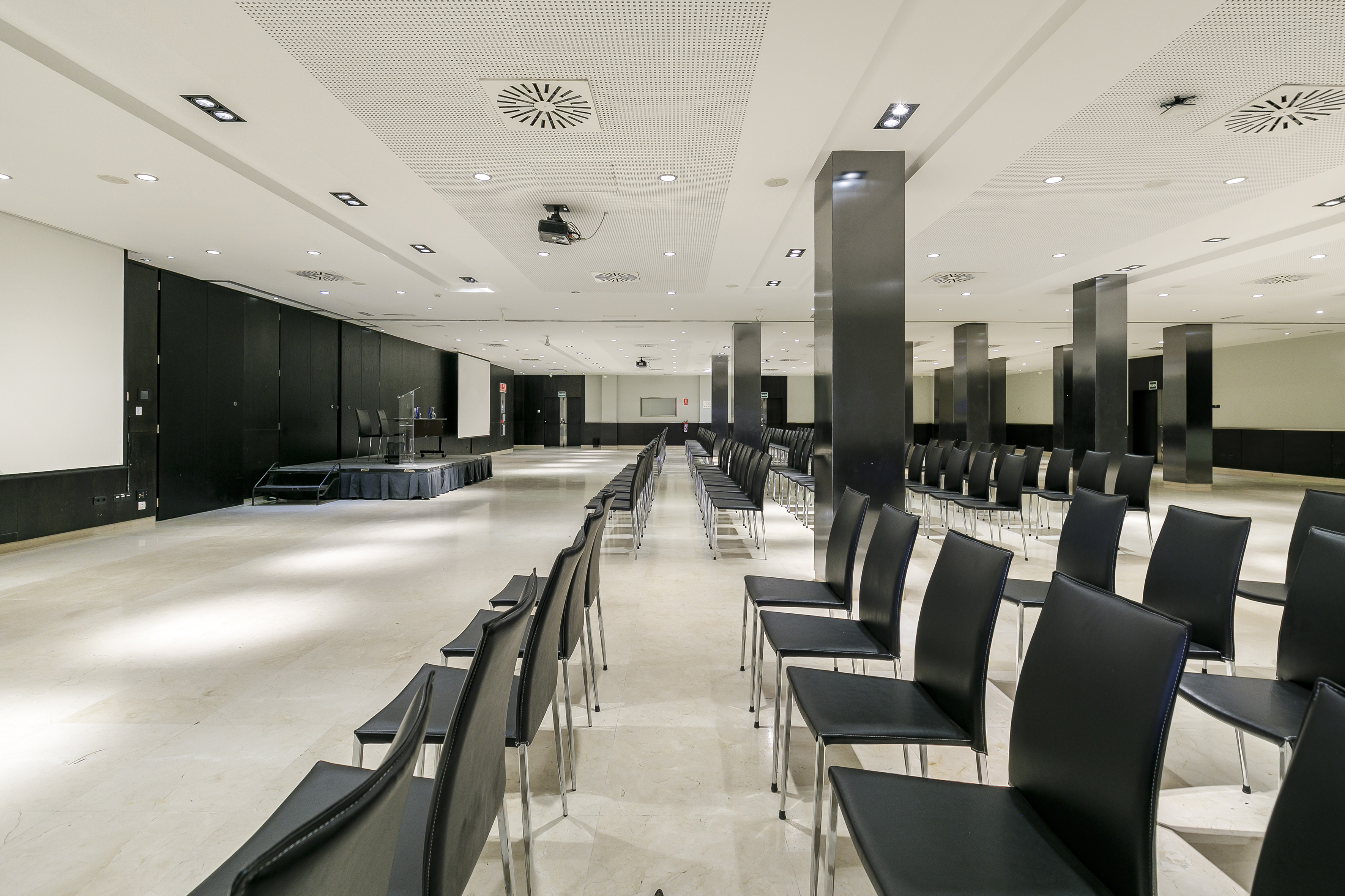 Modern conference room with empty black chairs, stage, and projector.