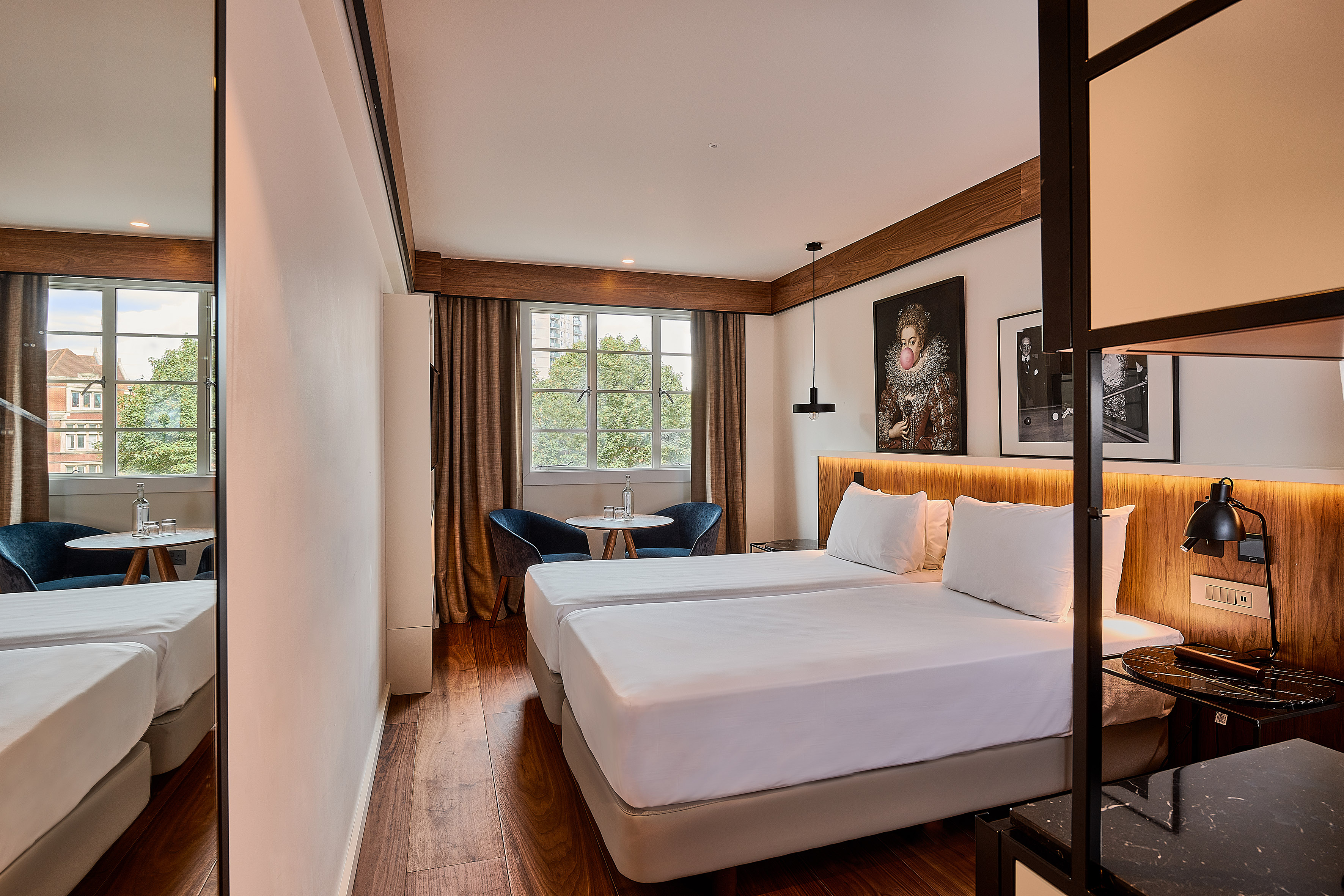 Modern hotel room with two single beds, wood floor, window, and wall art.