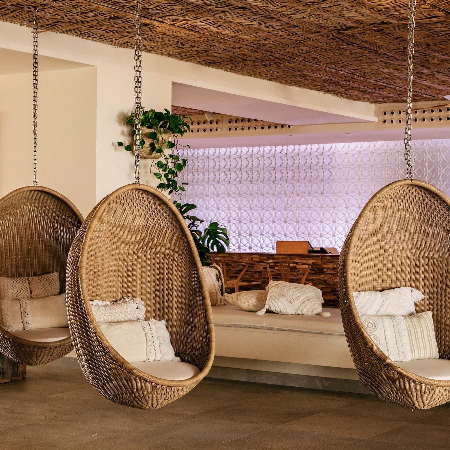 Tres sillas colgantes de mimbre con cojines en un lounge tropical.