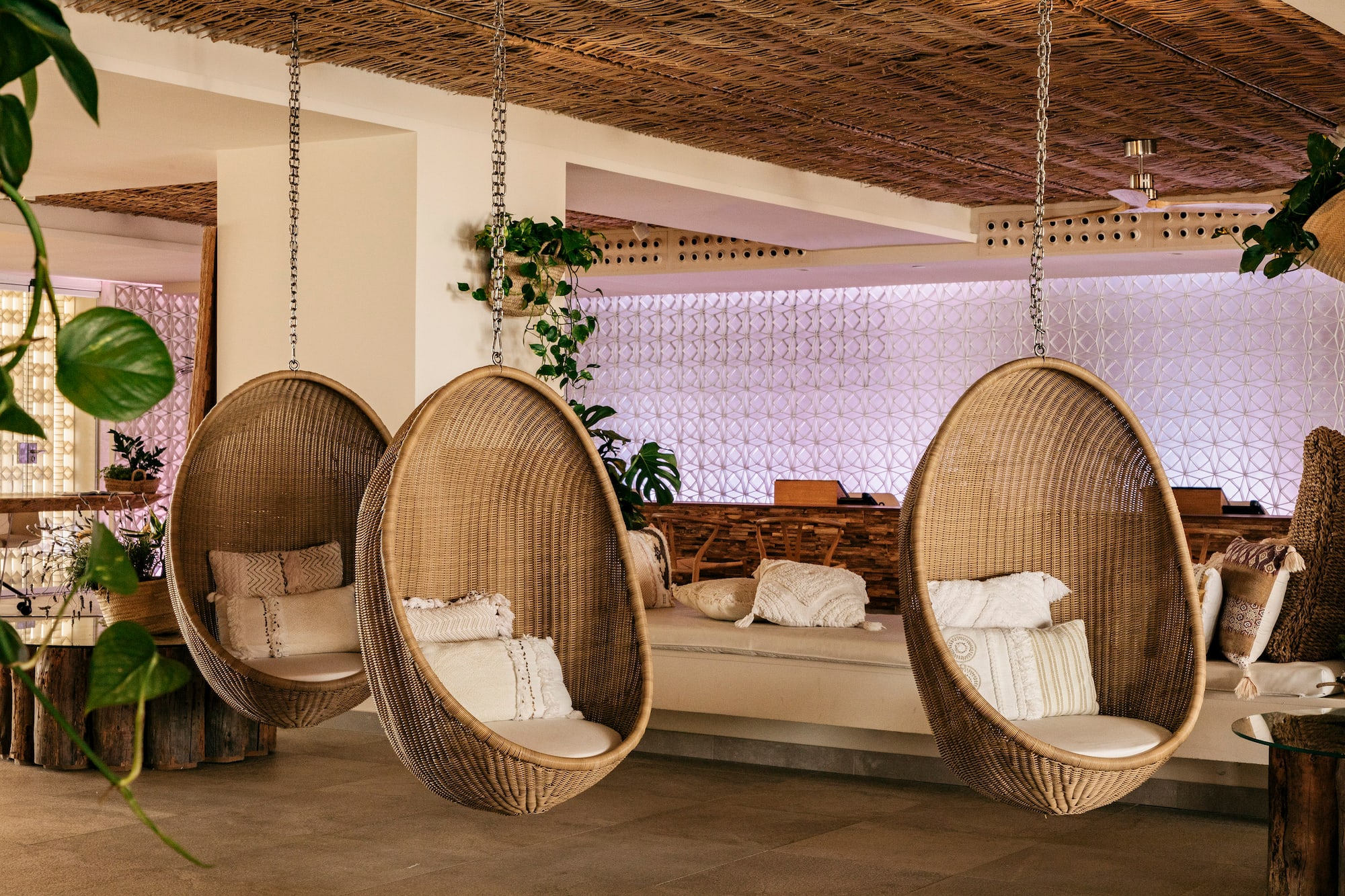 Three wicker hanging egg chairs with cushions in a stylish resort lounge.