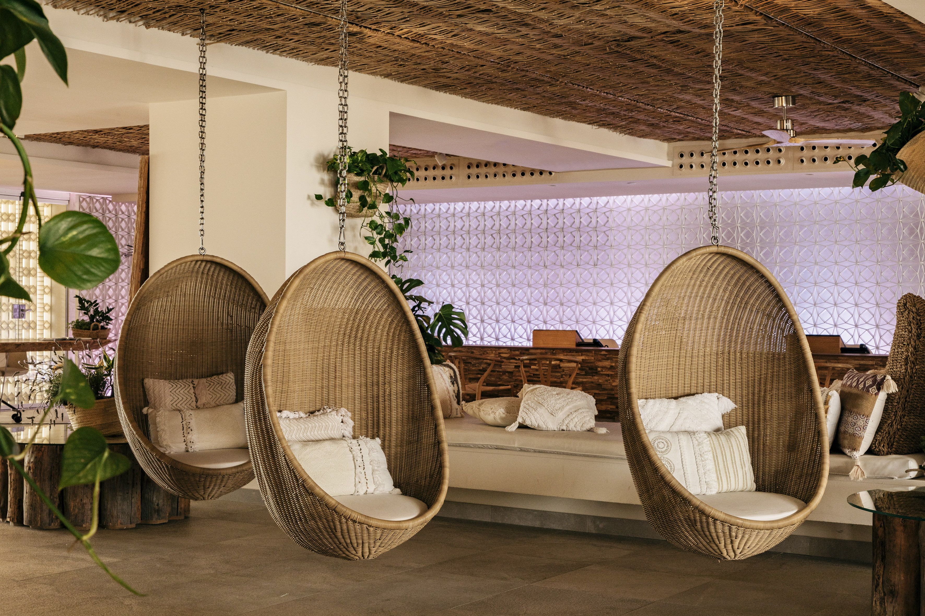 Tres sillas colgantes de mimbre con cojines en un lounge tropical.