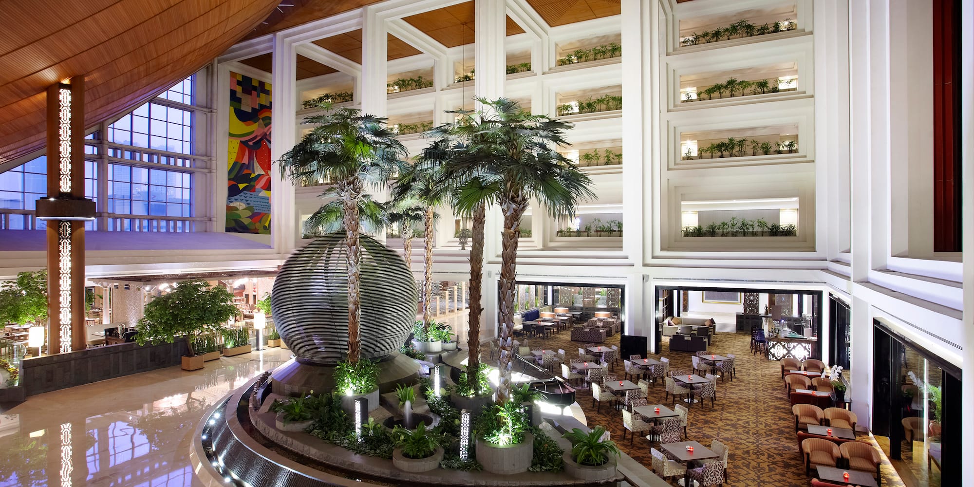 Spacious hotel lobby with palm trees, decorative fountain, and lounge seating.